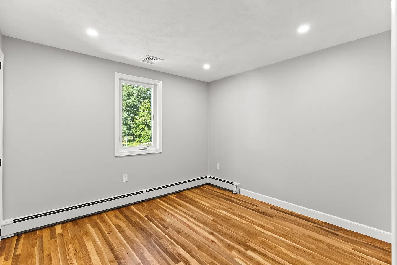 Empty room with hardwood floors, white walls, a small window, and ceiling lights.