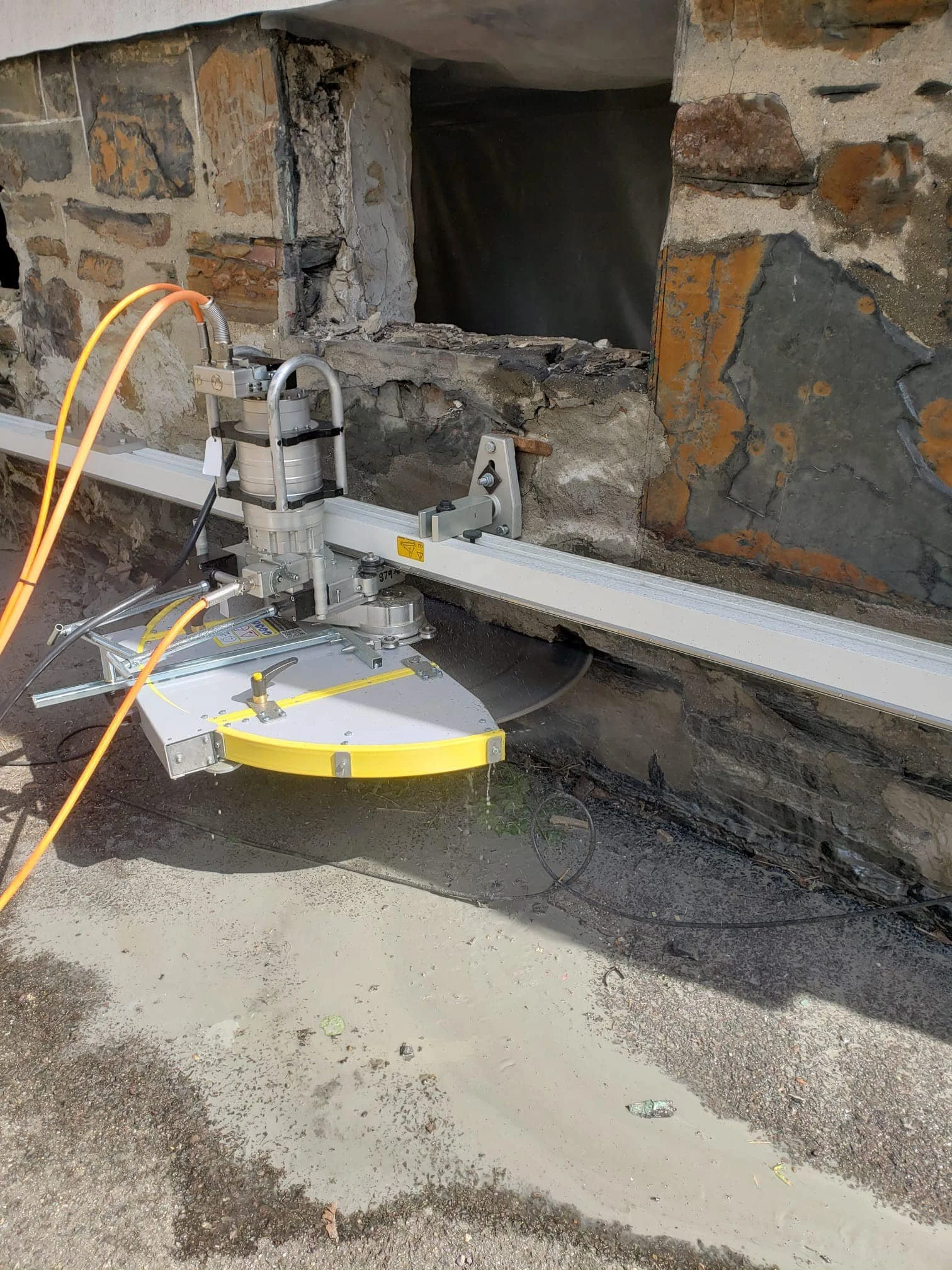 A construction site with a specialized stone-cutting machine near a stone wall with a large opening.