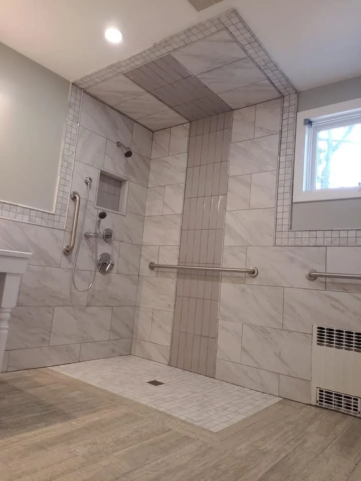 A wheelchair accessible shower with grab bars, a built-in niche, and a window in a tiled bathroom.