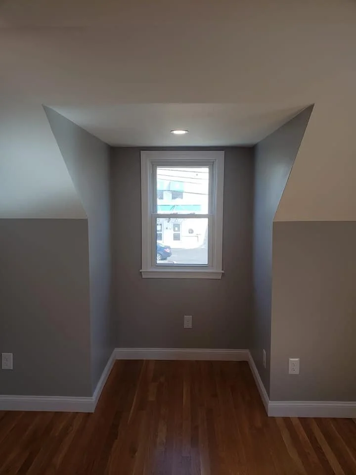 Small nook with a window, hardwood floor, gray walls, and white trim, with slope ceiling on both sides.