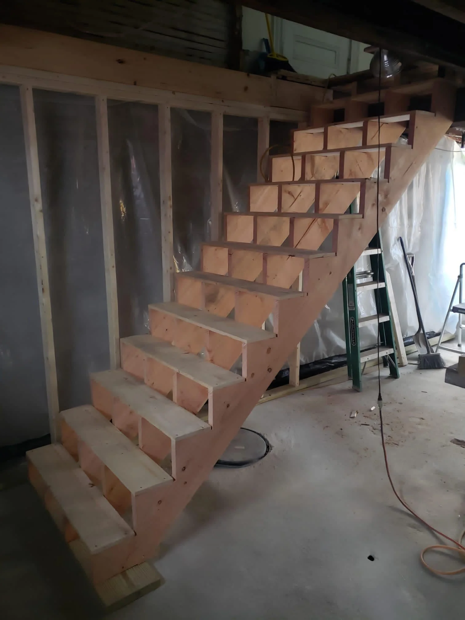 unfinished wooden staircase construction inside a building, with visible framing and tools nearby.