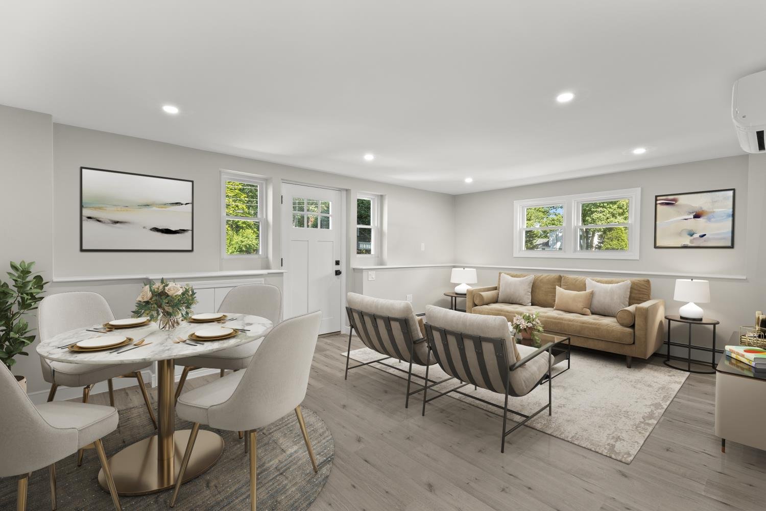 Living room and dining area with beige and gray furniture, abstract art on the walls, and large windows showing green trees outside.