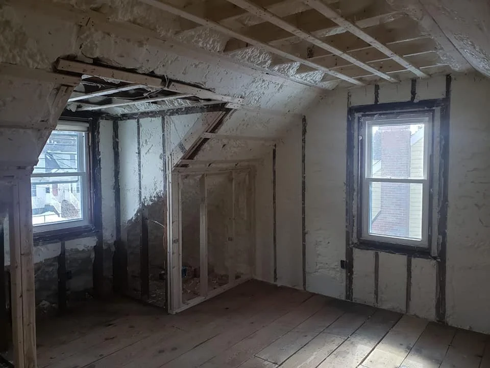 A room under construction with two windows, exposed wooden framing, and unfinished walls.