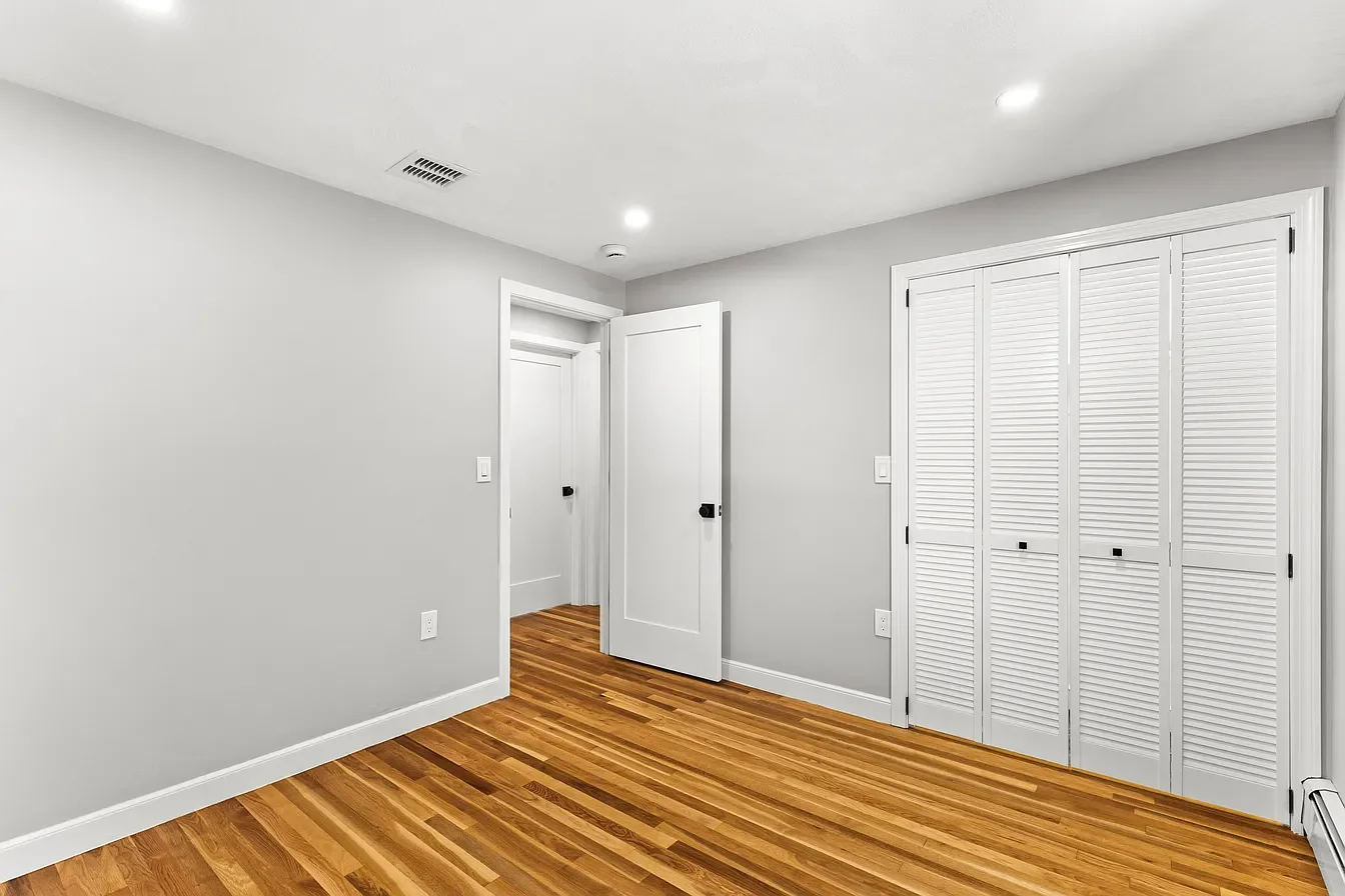 Empty room with light gray walls, white doors, wooden floor, and white louvered closet doors.