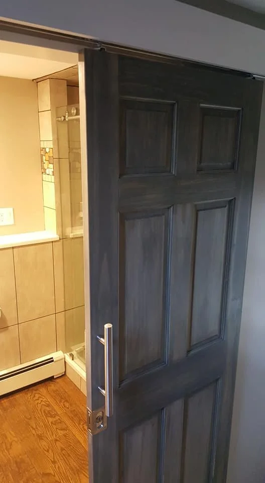 A partially open sliding bathroom door showing the shower area with tiled walls and a towel bar.