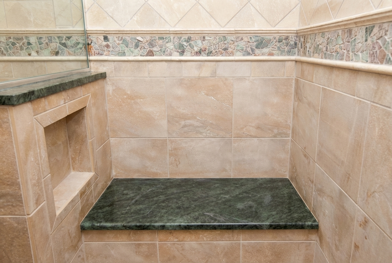 Close-up of a shower corner with beige tiles, a small built-in shelf, and a dark green marble bench.