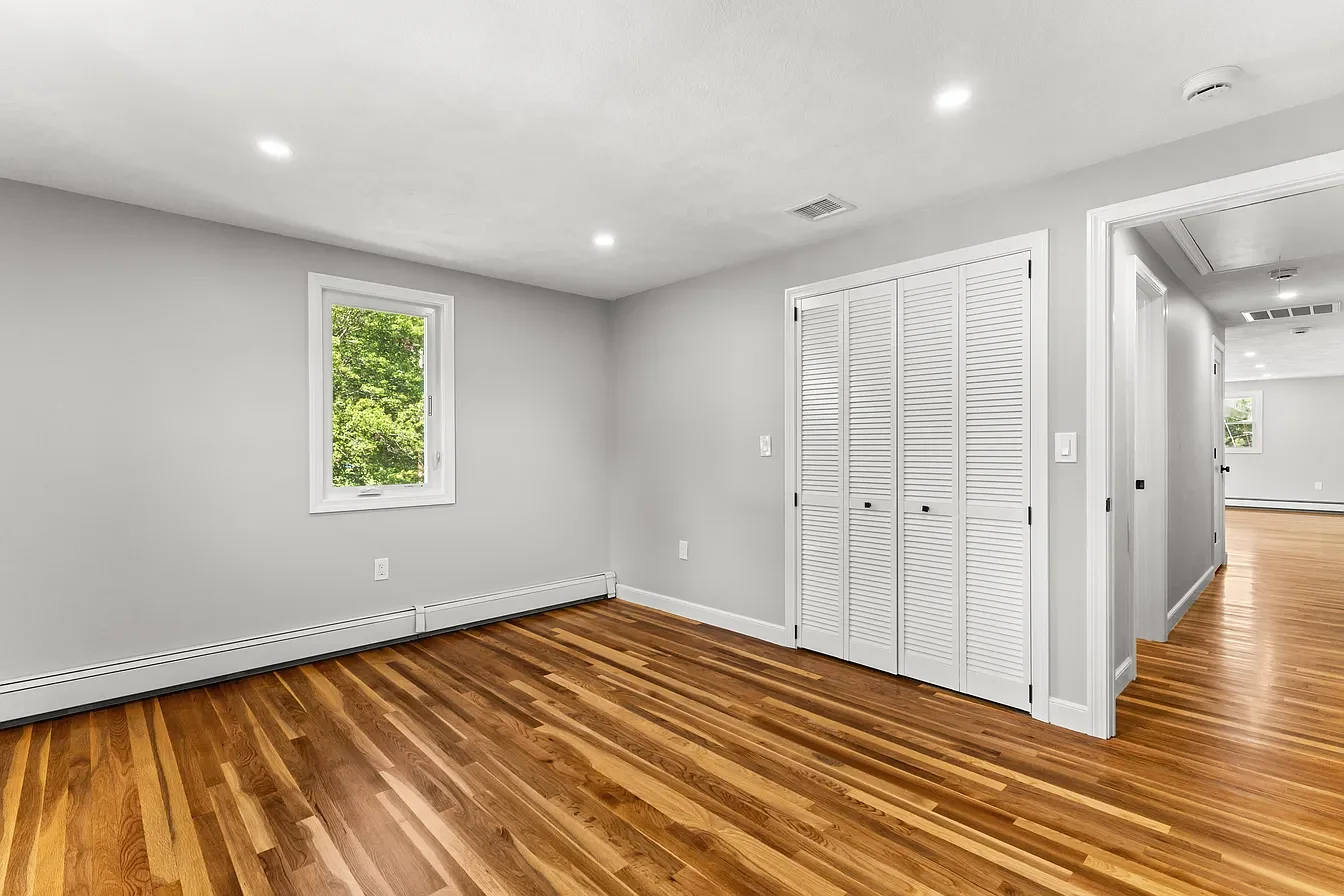 Empty room with hardwood floors, white walls, a small window, and a closet with louvered doors.