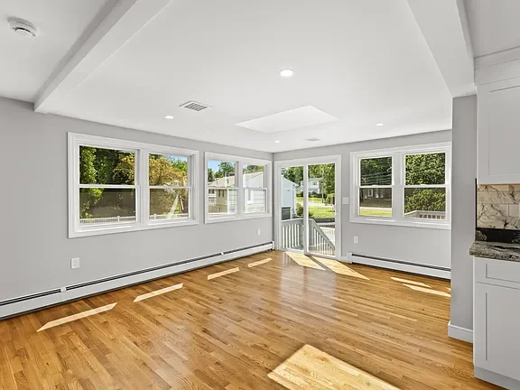 Empty living room with hardwood flooring and multiple large windows letting in natural light.