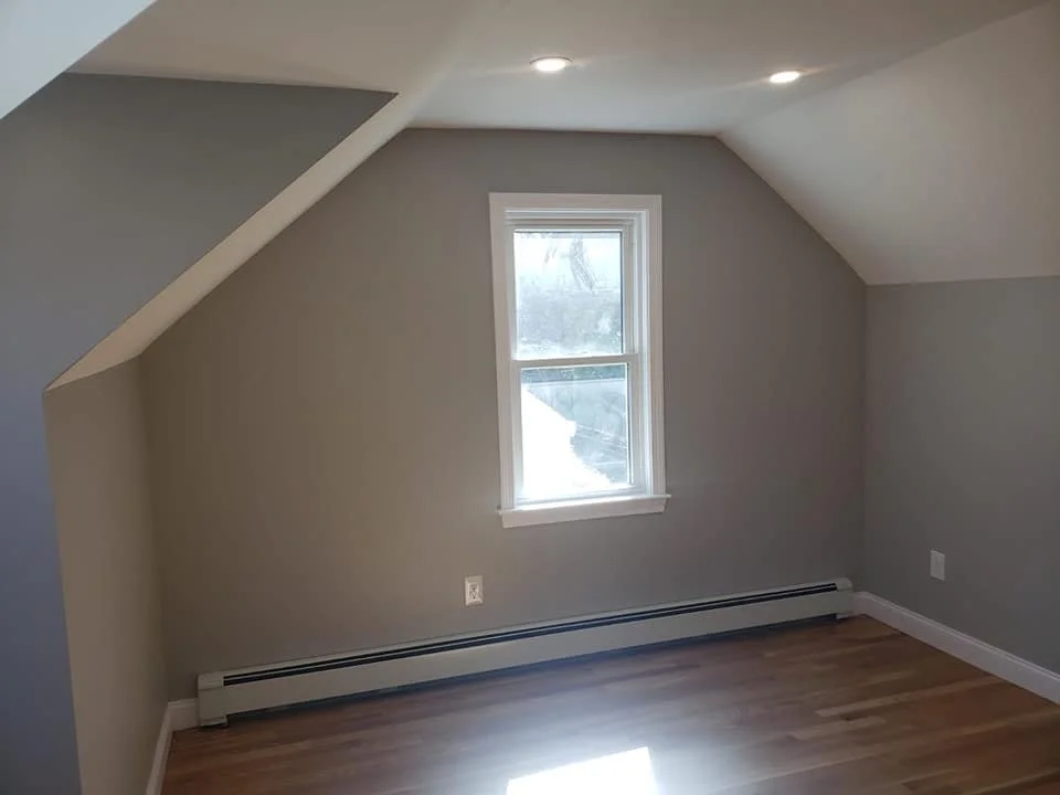 Empty room with gray walls, a single window, hardwood floor, and ceiling lights.