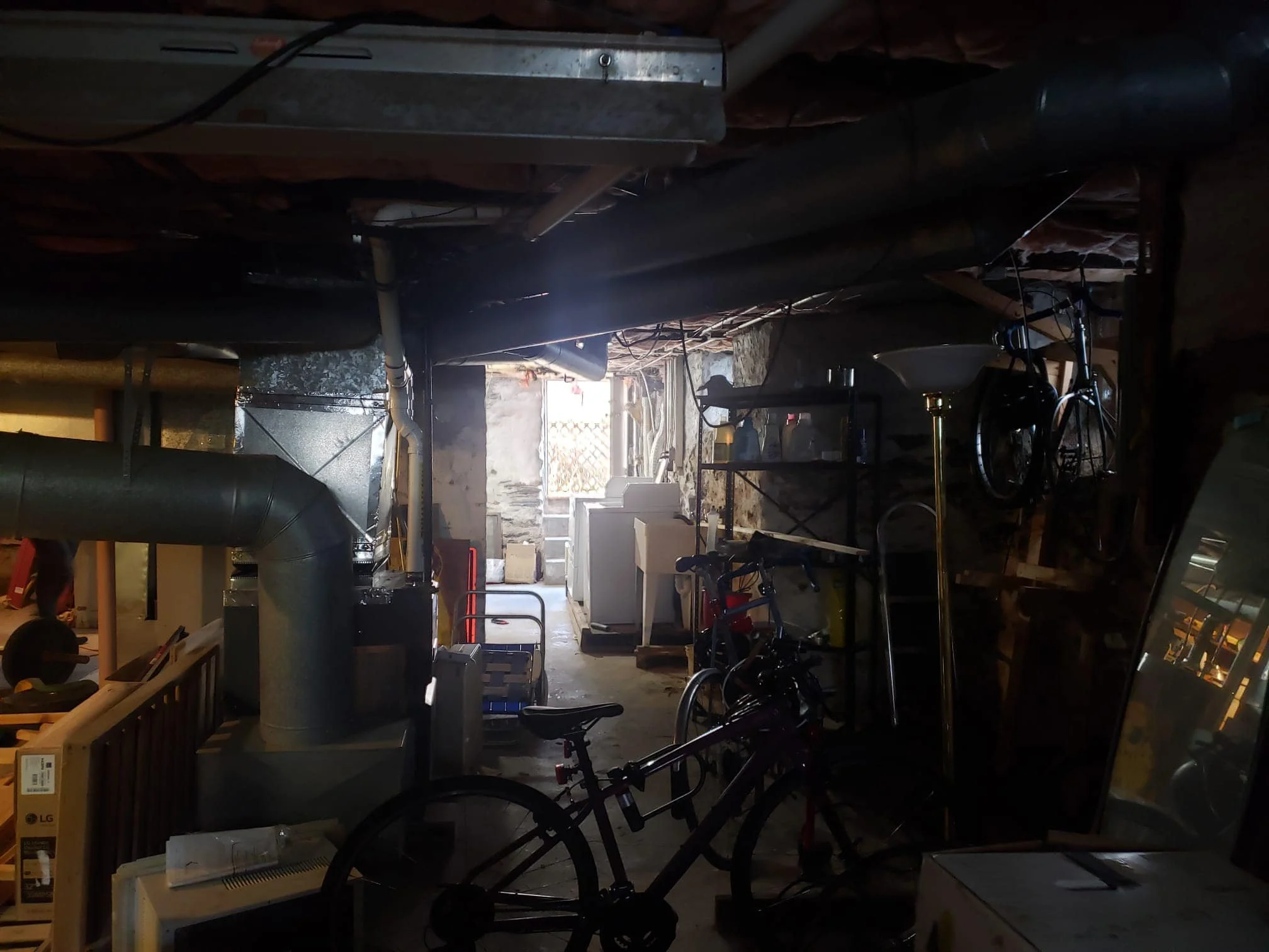 A cluttered basement with various objects including bicycles, a mirror, and appliances, with an open door leading outside.