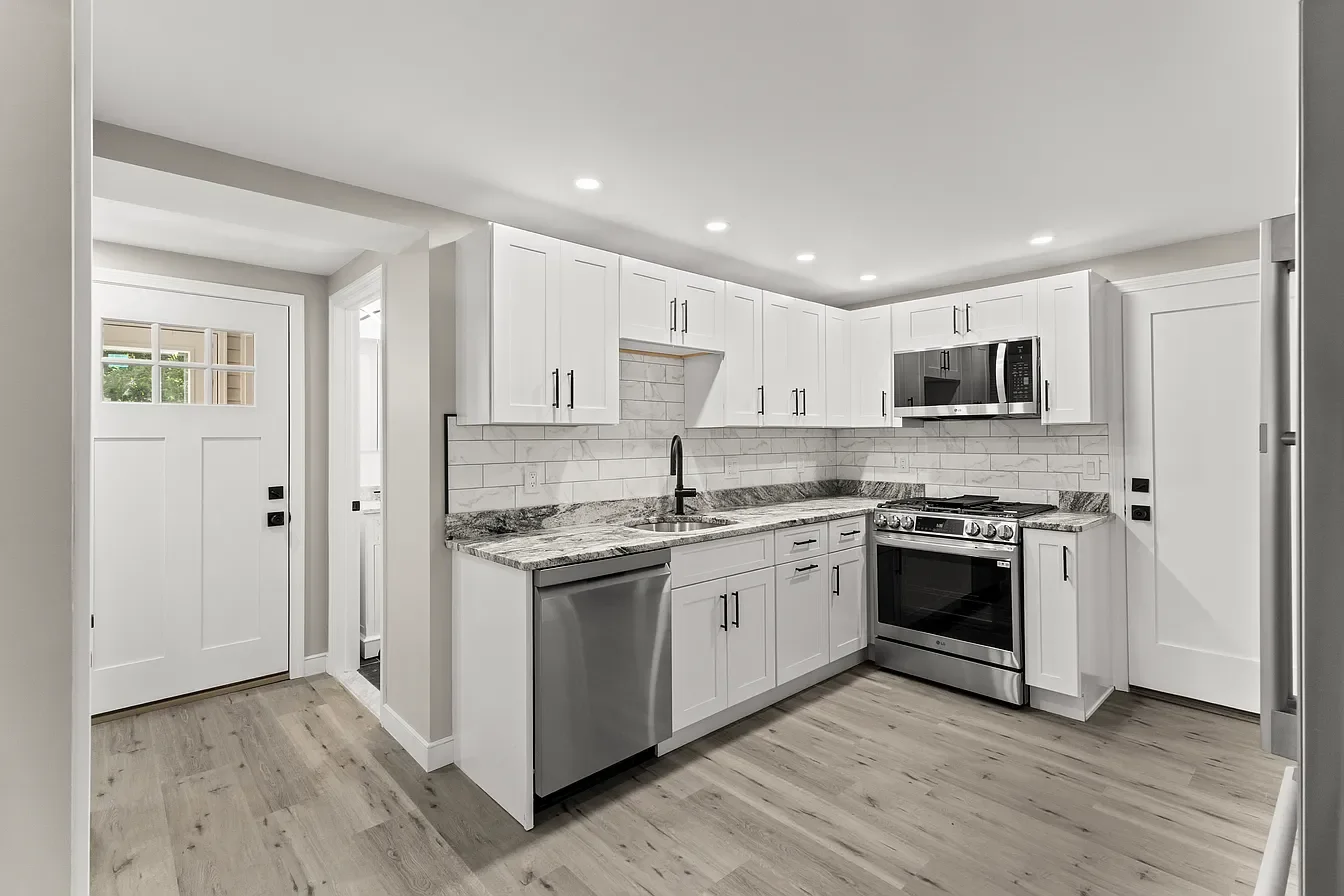 Modern kitchen with white cabinets, granite countertop, stainless steel appliances including microwave, oven, and dishwasher, and wood flooring.