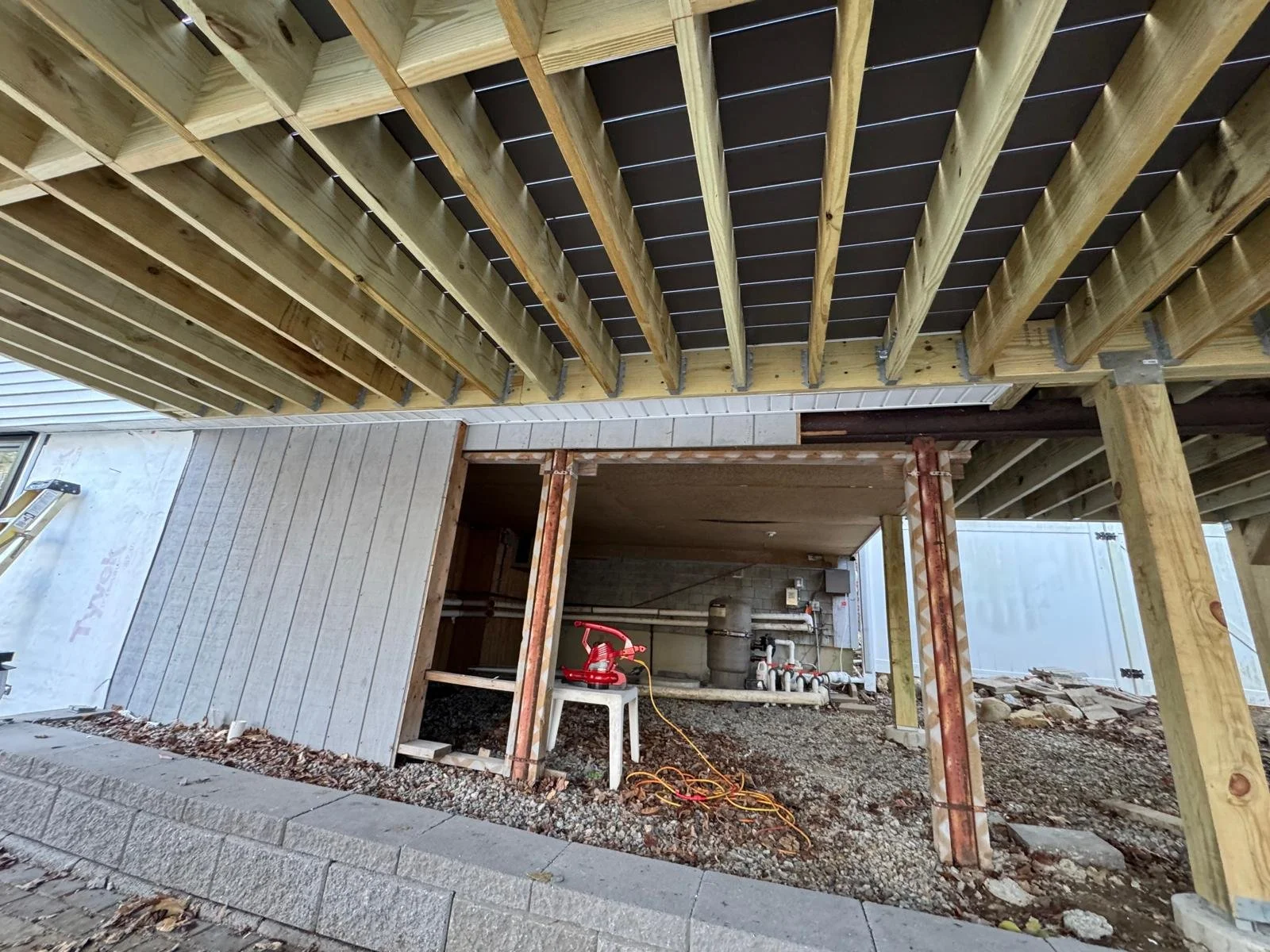 Under construction view of a building with exposed wooden beams, partially finished walls, and construction tools and materials such as a red water pump and electrical cords on the ground.