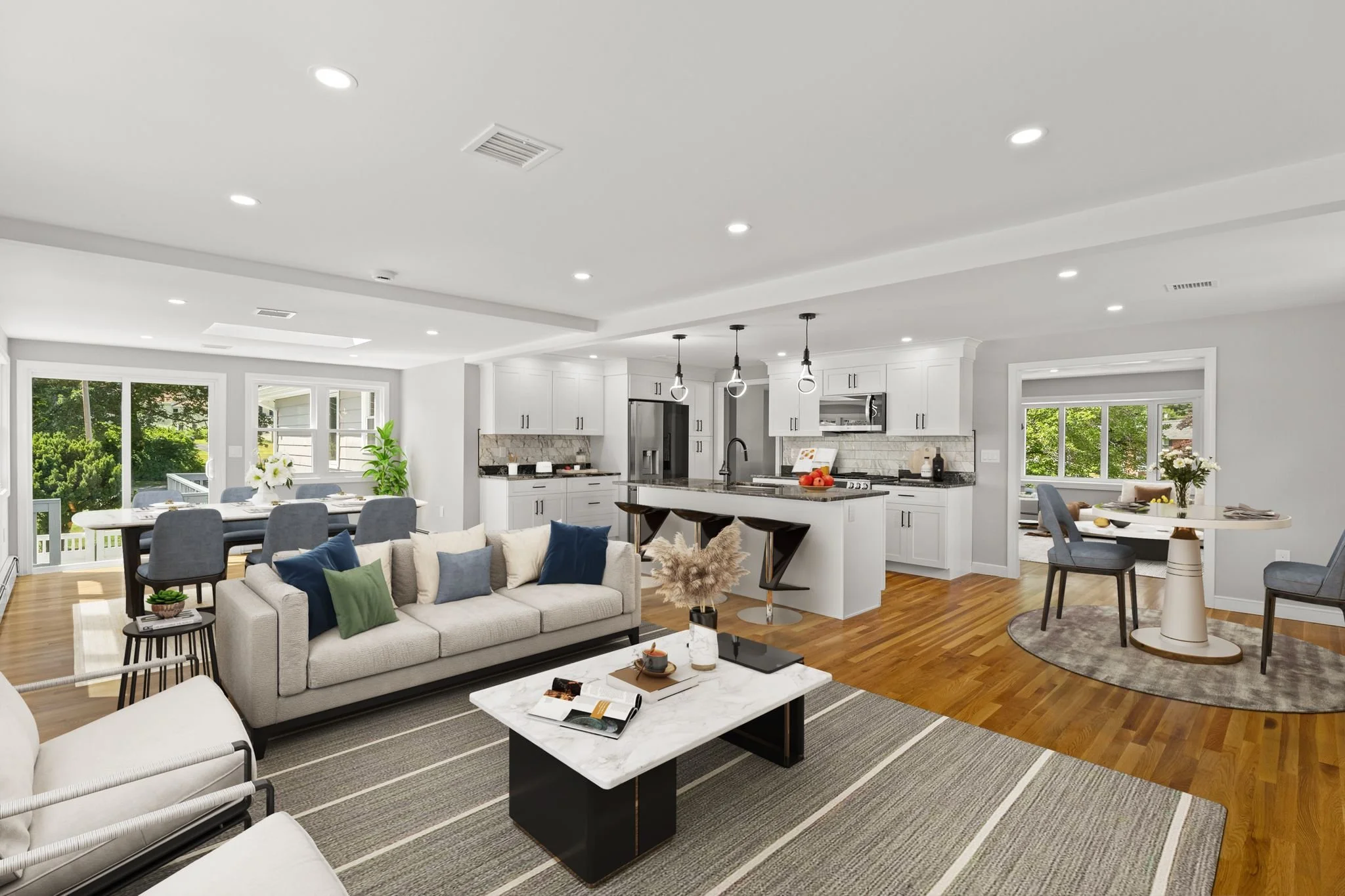 A spacious open-concept living room and kitchen with white walls and ceiling, hardwood floors, modern furniture, and large windows letting in natural light.