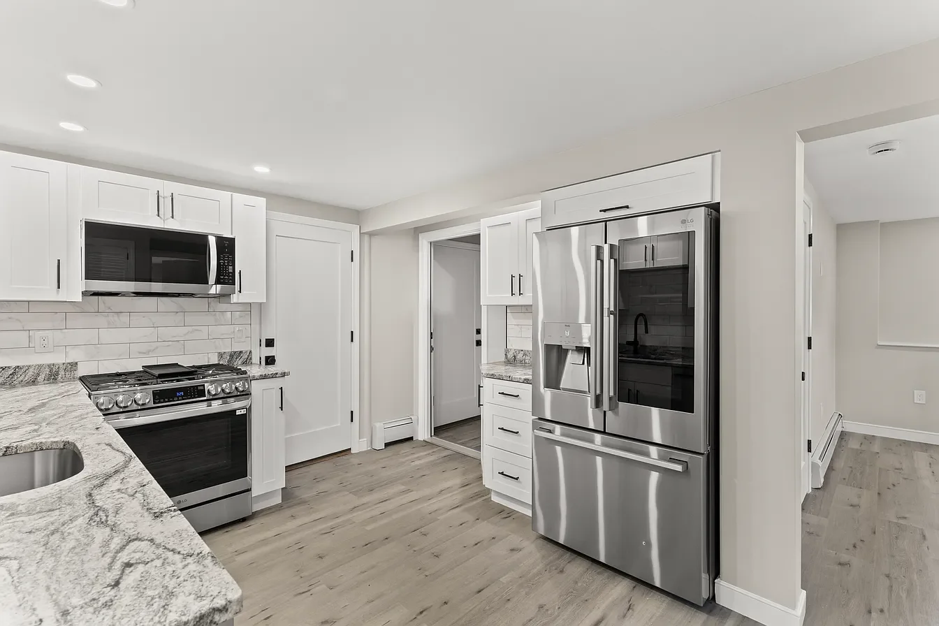 Modern kitchen with white cabinets, stainless steel appliances, granite countertops, wooden flooring, and recessed lighting.