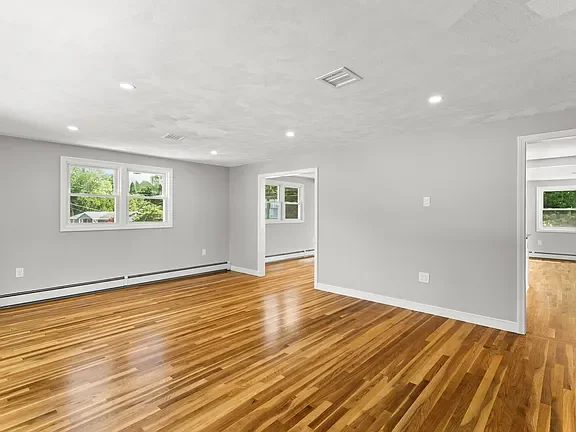 Empty living room with hardwood floors, gray walls, and multiple windows