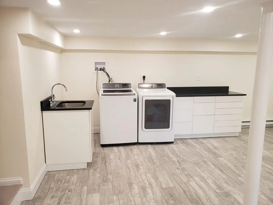 Laundry room with a white washing machine and dryer, a black countertop, and a white cabinet with a sink and faucet.