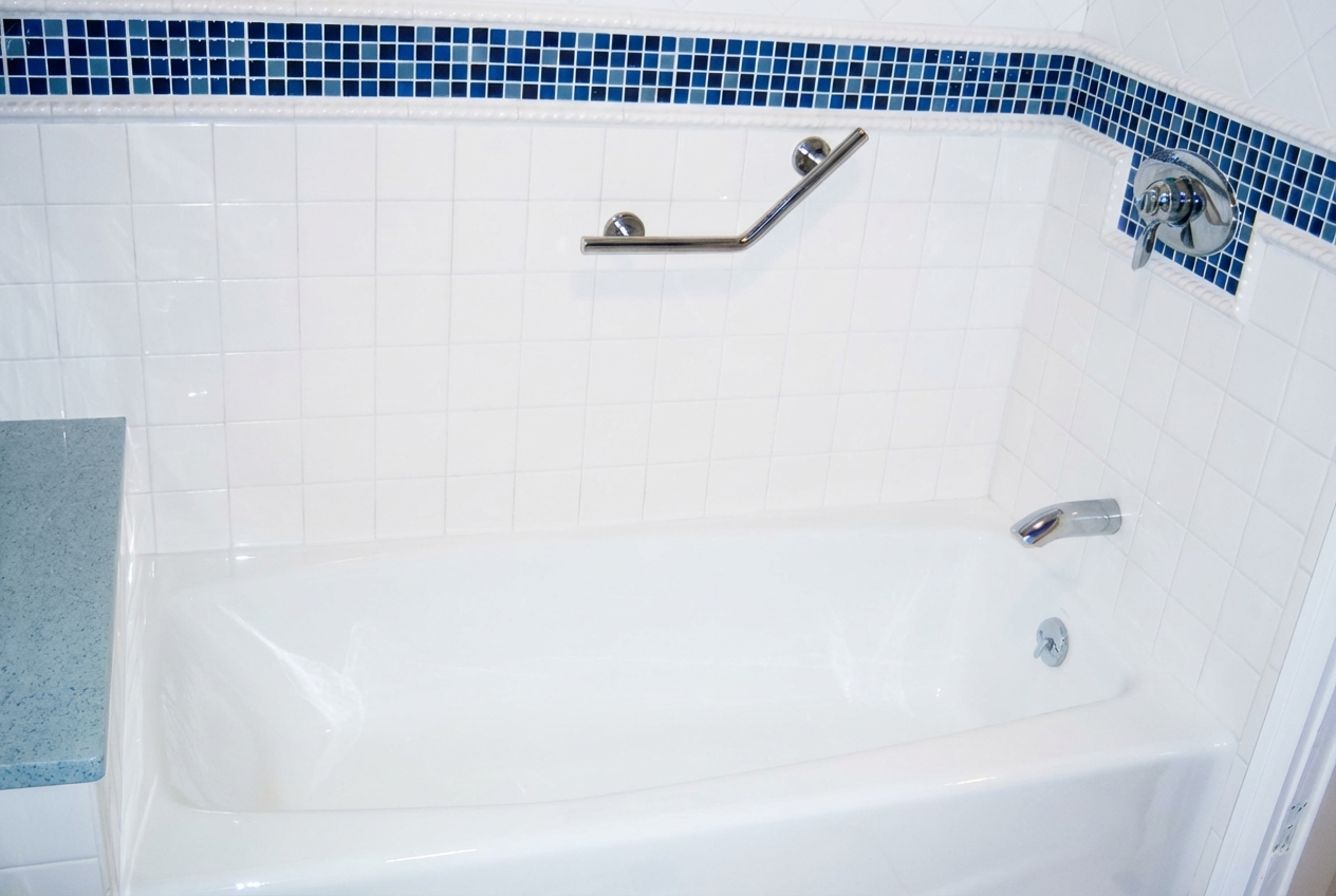 Empty white bathtub with blue mosaic tile border, silver grab bar, faucet, and showerhead in a bathroom.