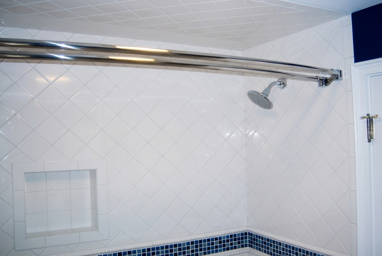 Shower area with white tiled walls, a showerhead, and a curved shower curtain rod.