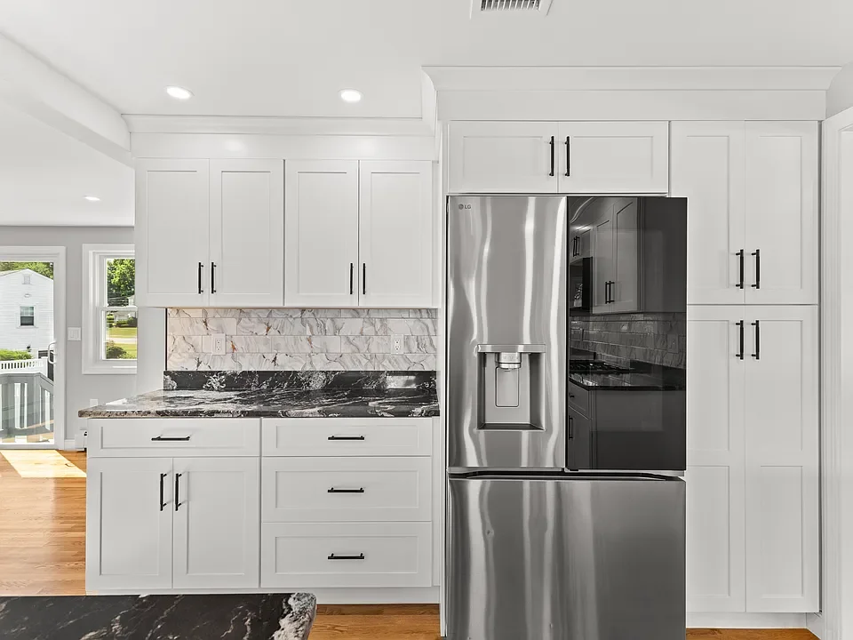 Modern kitchen with white cabinets, black hardware, marble backsplash, and stainless steel LG refrigerator.