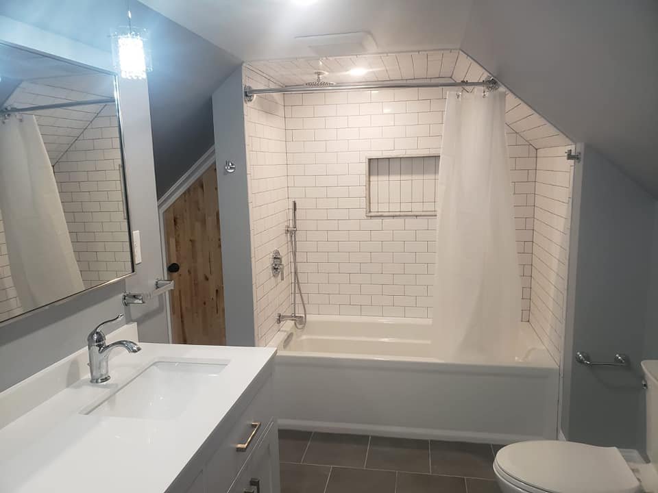A modern bathroom with a white vanity and sink, a large mirror, a bathtub with a shower curtain, white tile walls, and a gray tile floor.