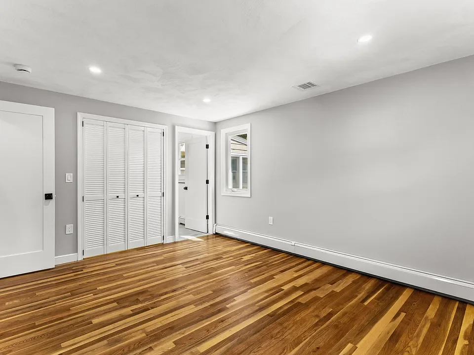 Empty room with hardwood floors, white walls, a window, and a closet with louvered doors.