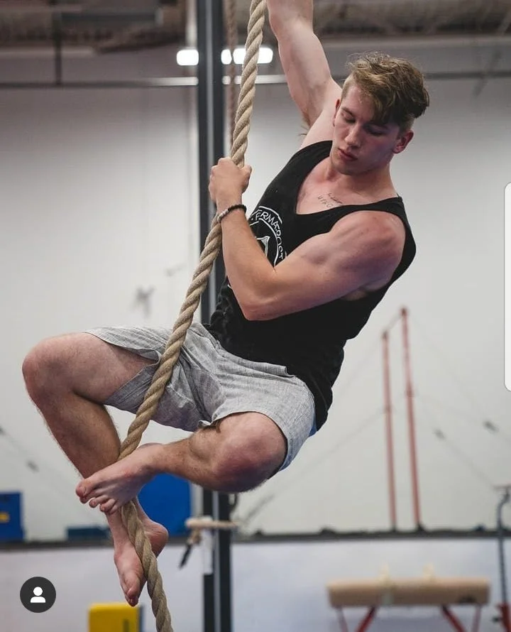 Young man climbing a thick rope in an indoor gym.