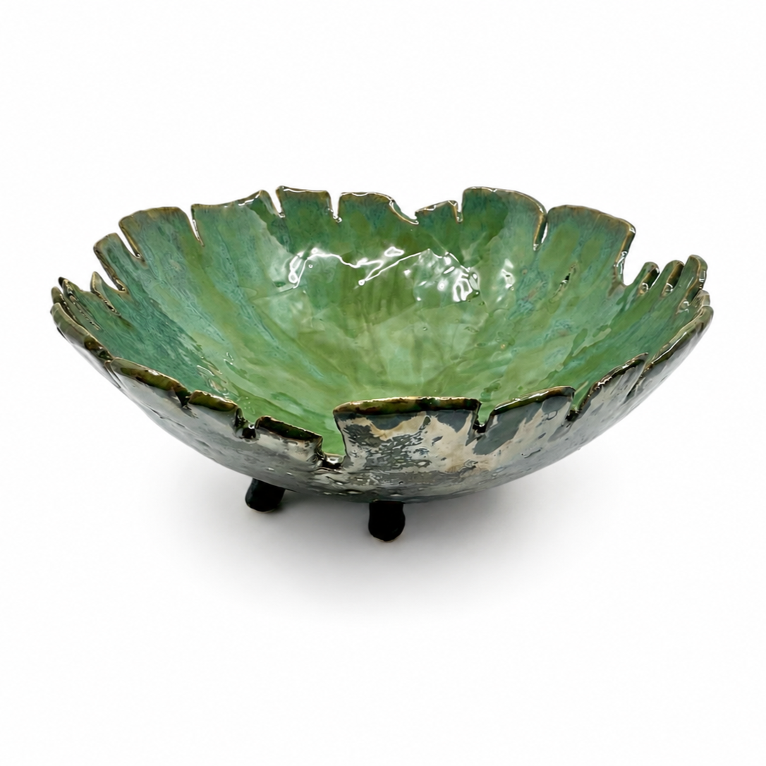 Green ceramic bowl with irregular edges and small legs, glossy finish, on a white background.
