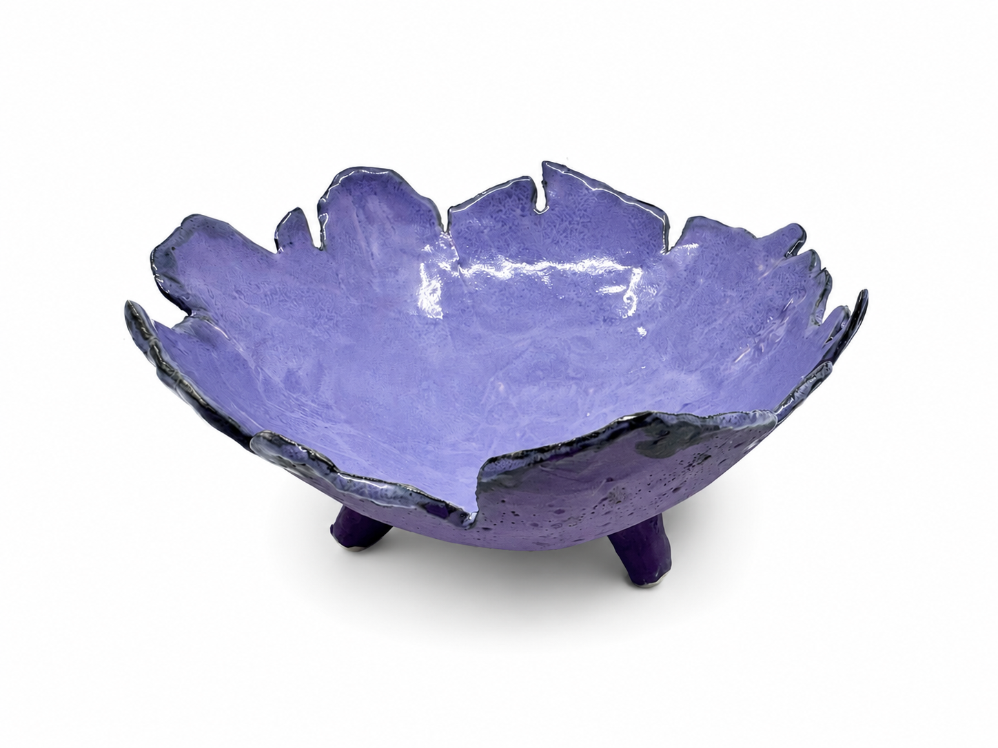 Purple decorative bowl with uneven, petal-like edges and three small legs, isolated on white background.
