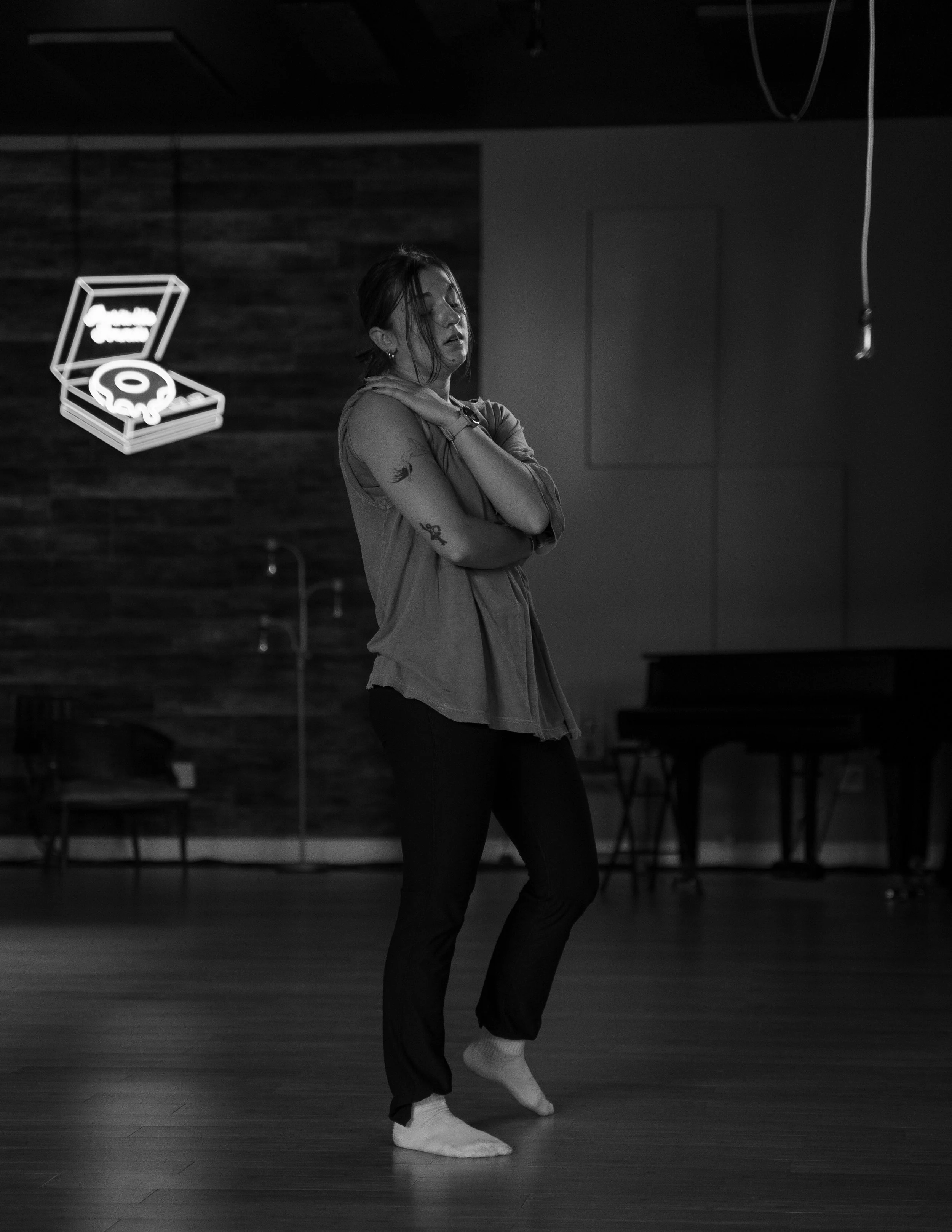 gabby dancing barefoot in a dimly lit room, with a neon record player sign on the wall behind her.