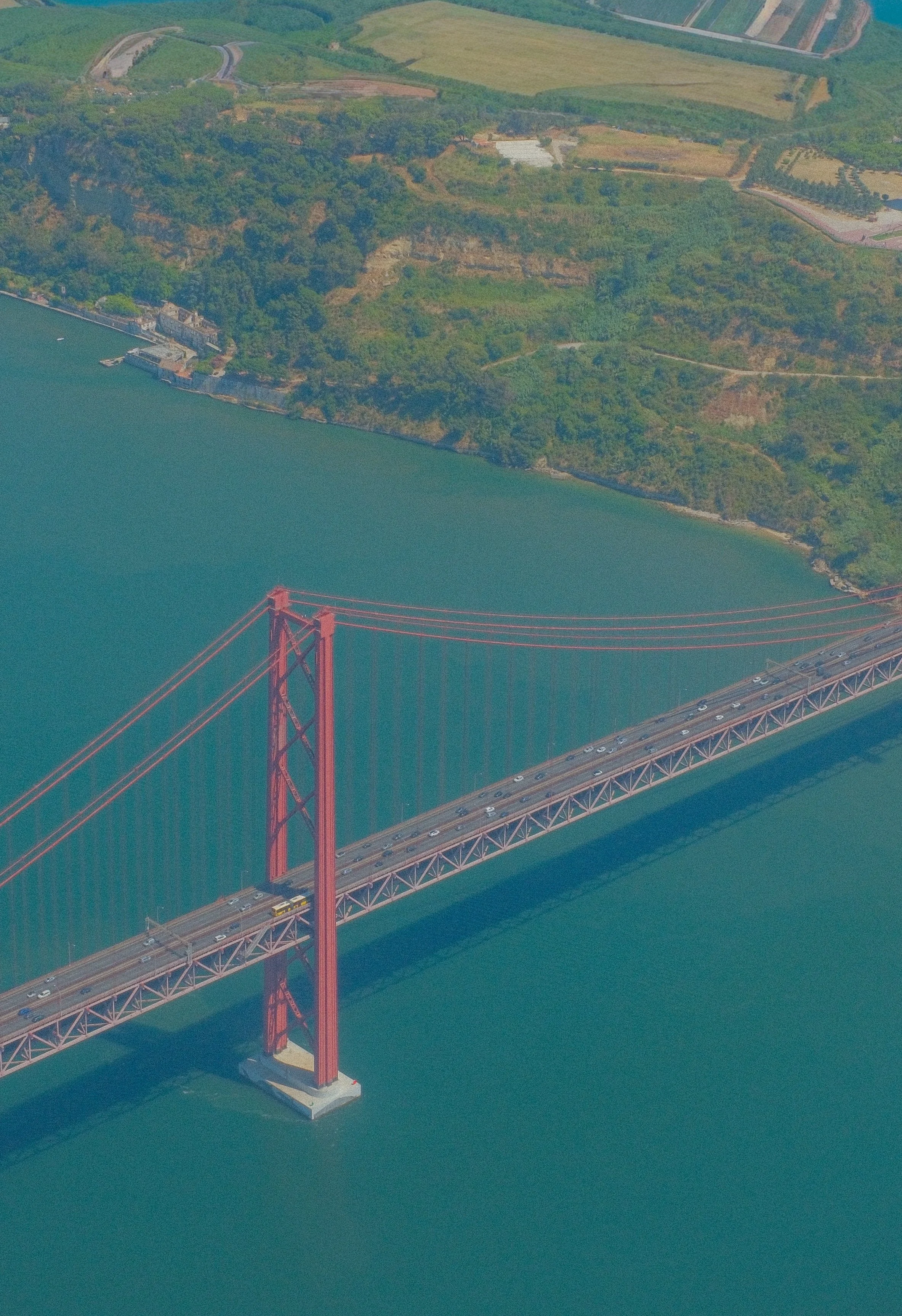 Aerial view of the Golden Gate Bridge over water, with a lush green landscape and hills in the background.