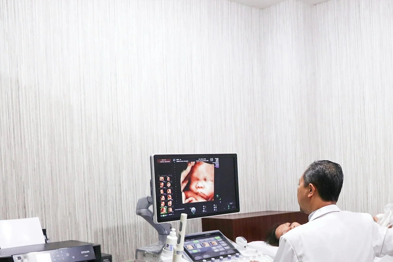 Medical professional performing an ultrasound scan of a pregnant woman's abdomen, with the ultrasound monitor displaying a 3D image of the fetus.