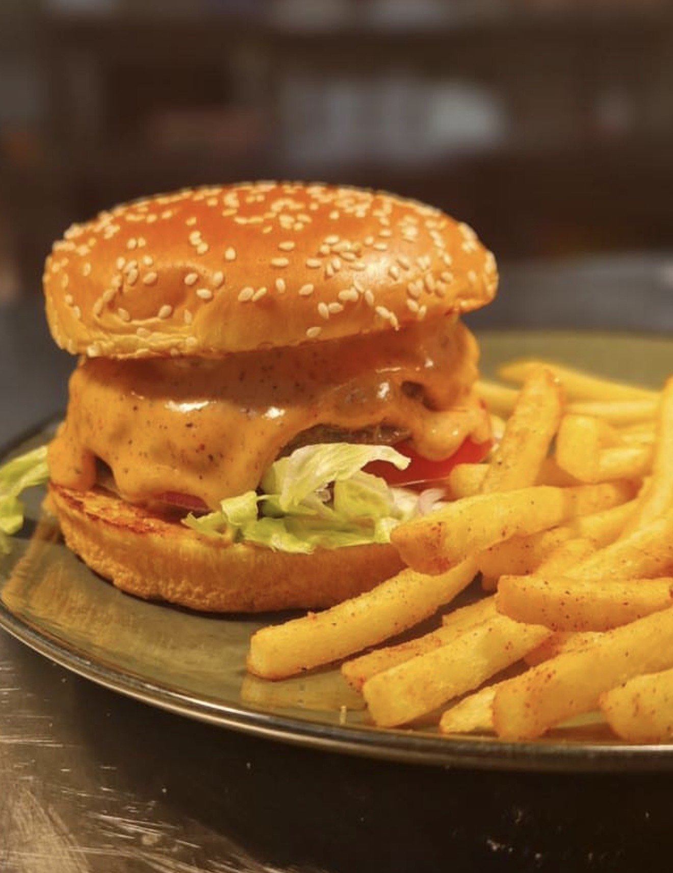 A cheeseburger with lettuce, tomato, pickle, and melted cheese on a sesame seed bun, served with seasoned French fries on a plate.