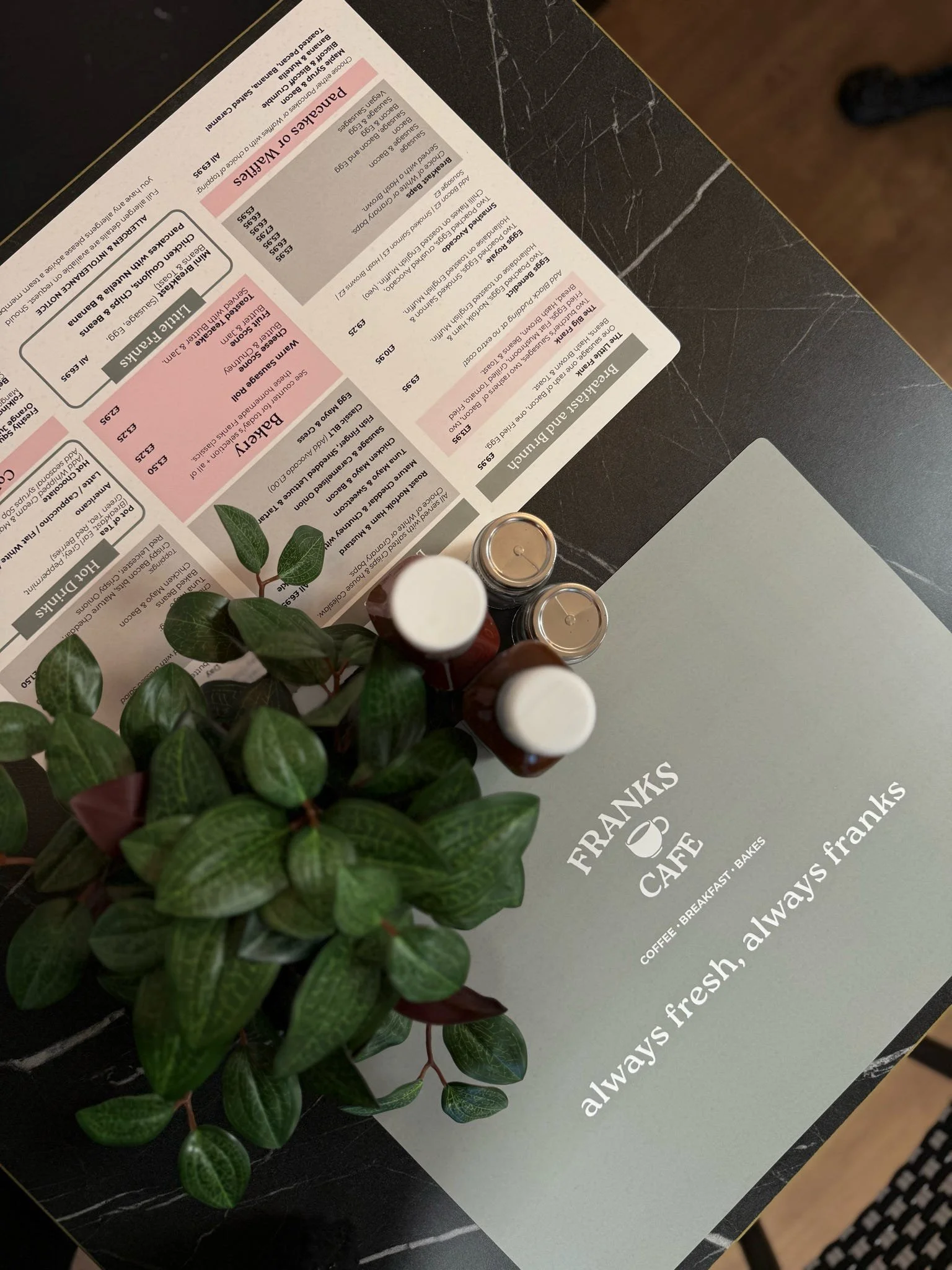 Table at Frank's Cafe with a menu, small potted plant, and three bottles of sauces.
