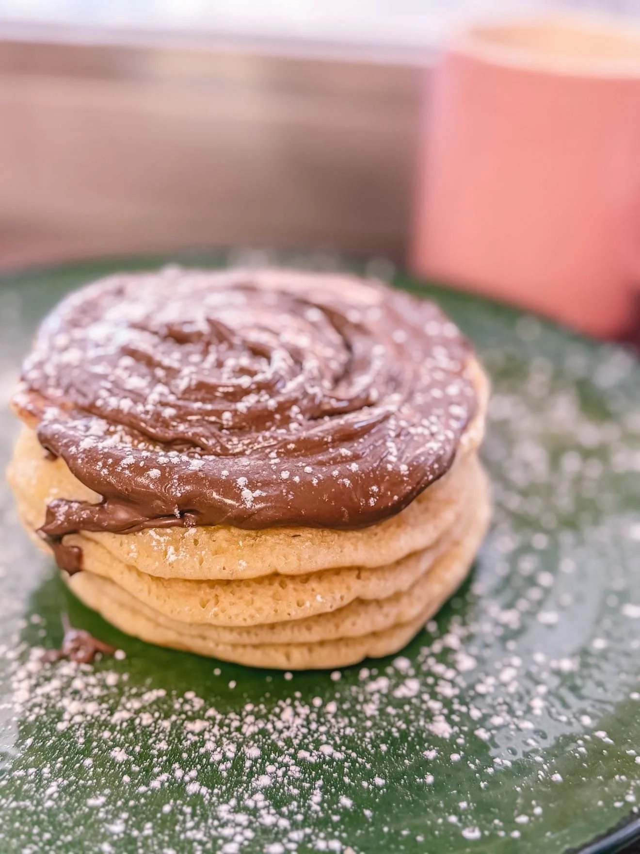 Stack of four cookies with chocolate frosting on top, dusted with powdered sugar, on a green leaf, with a pink and tan background.