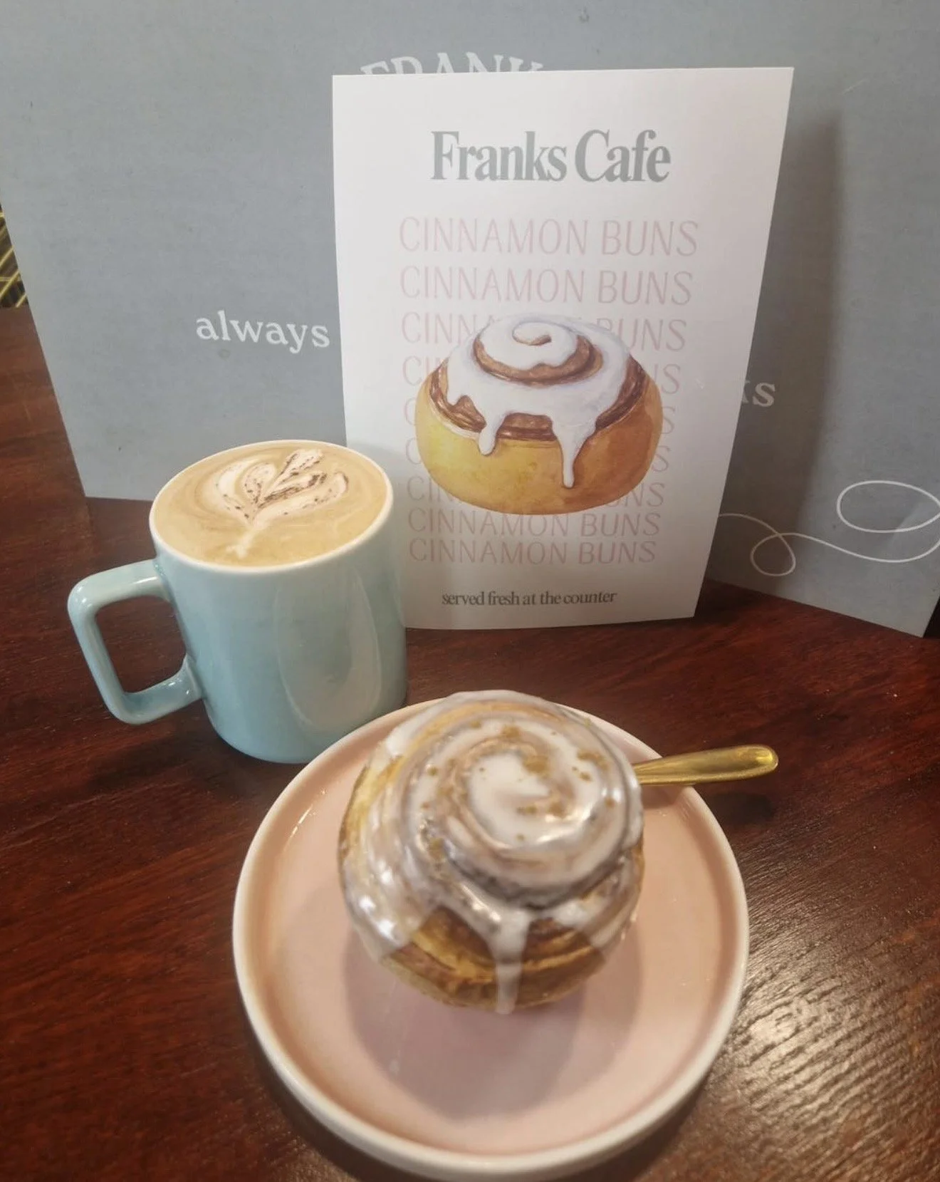 Cup of latte with latte art, cinnamon bun with icing, cinnamon bun menu with cinnamon buns, displayed at a cafe.
