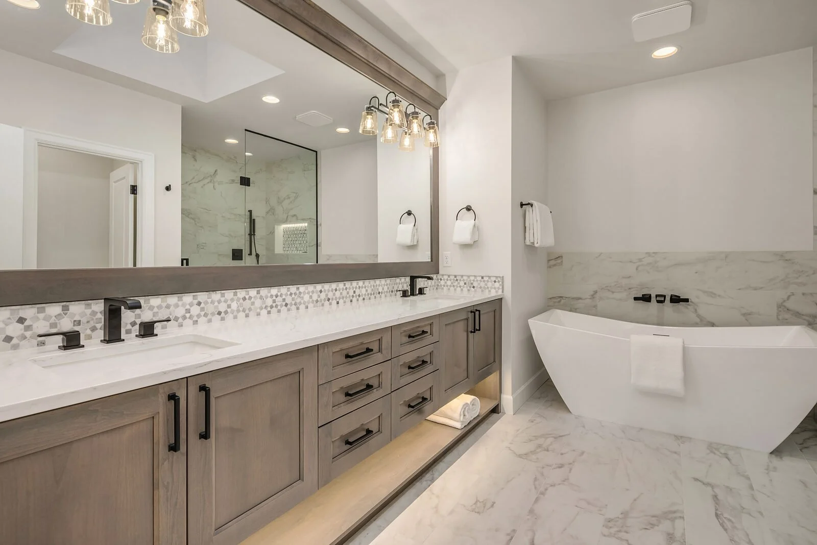 Modern bathroom with double vanity, large mirror, hexagonal tile backsplash, and a freestanding bathtub with marble accents.