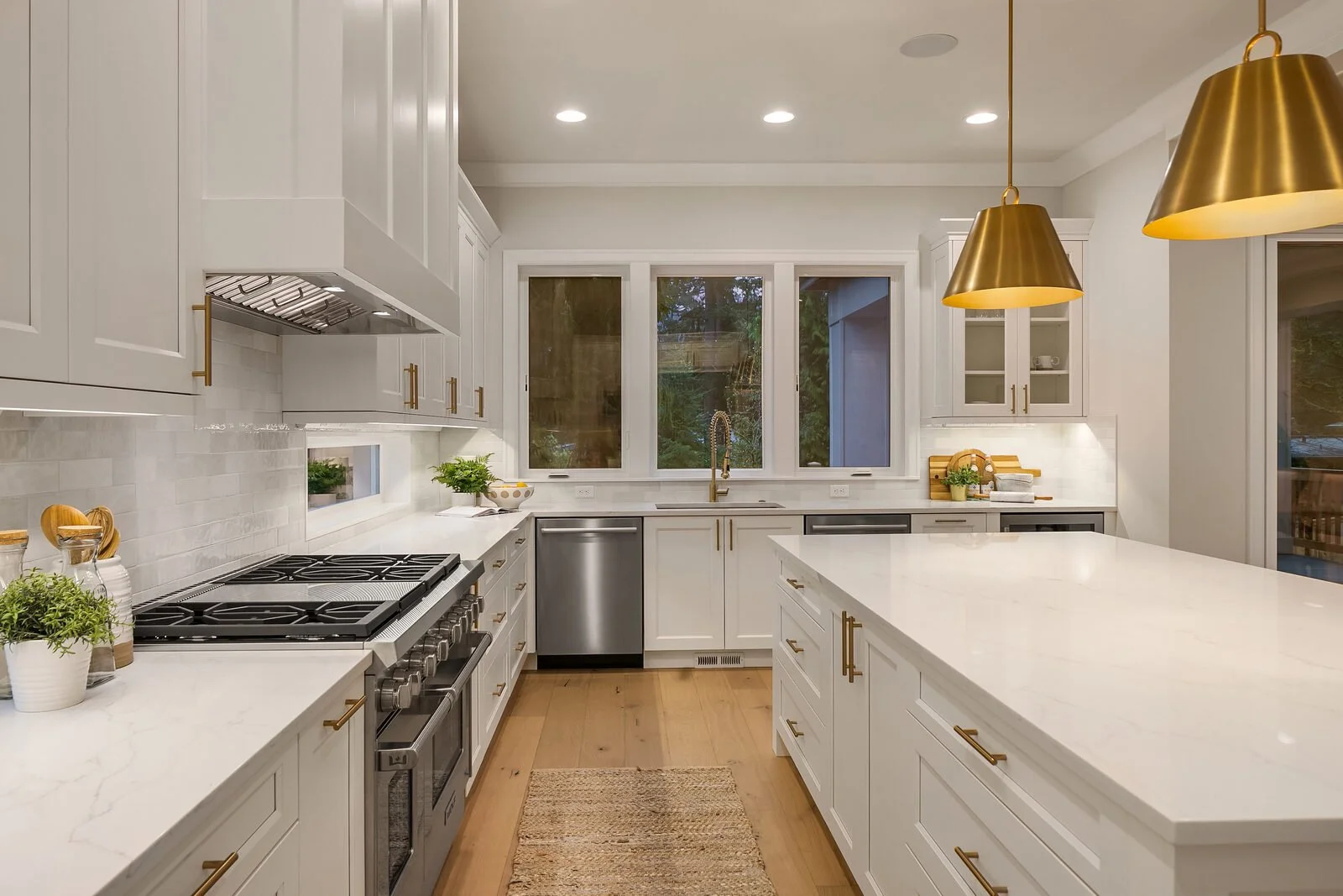 Modern white kitchen with gold hardware, stainless steel appliances, black stove, white marble countertops, and pendant lighting.