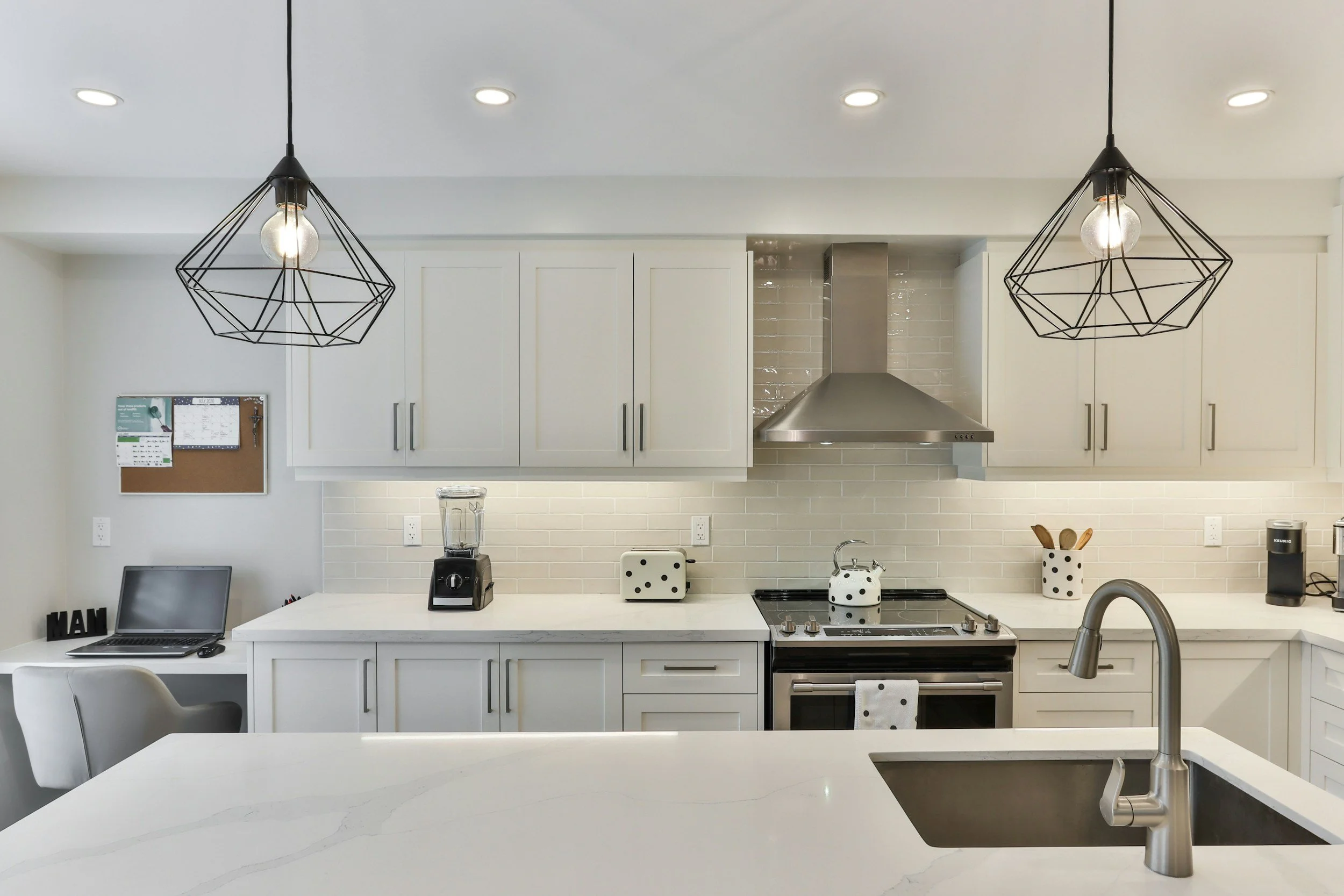 Modern white kitchen with pendant lights, stainless steel stove and hood, white cabinets, marble countertop, and black and white dotted kitchen accessories.