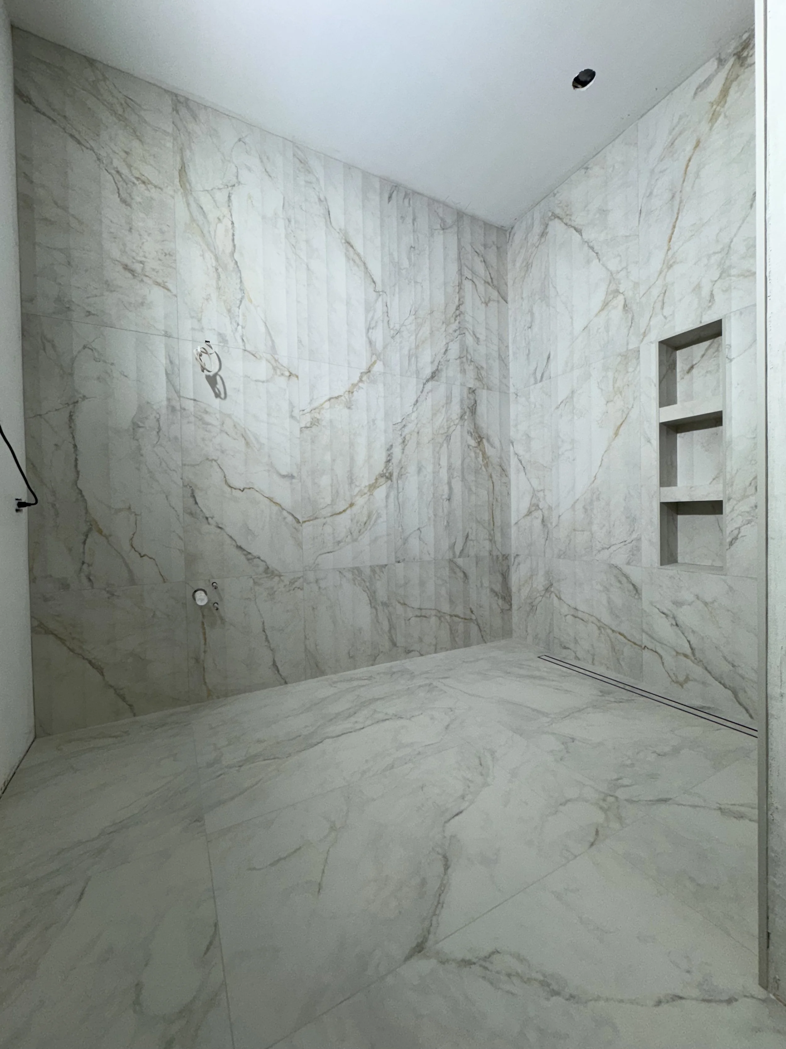 Empty walk-in shower with marble tiles on walls and floor, built-in wall niches, and a linear drain on the floor.