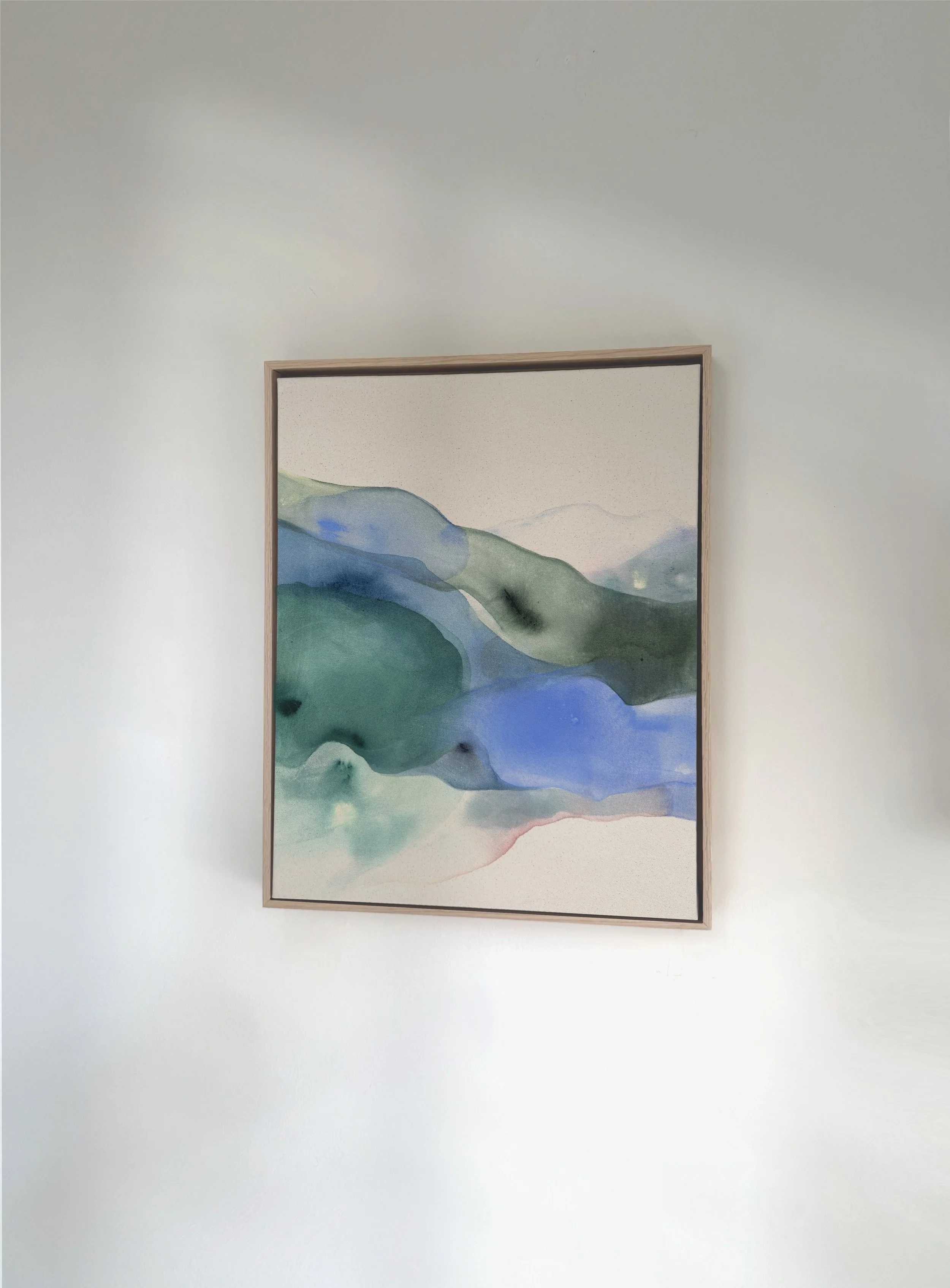 An abstract landscape painting of mountains and water in pastel and earth tones, framed and hanging on a beige wall.