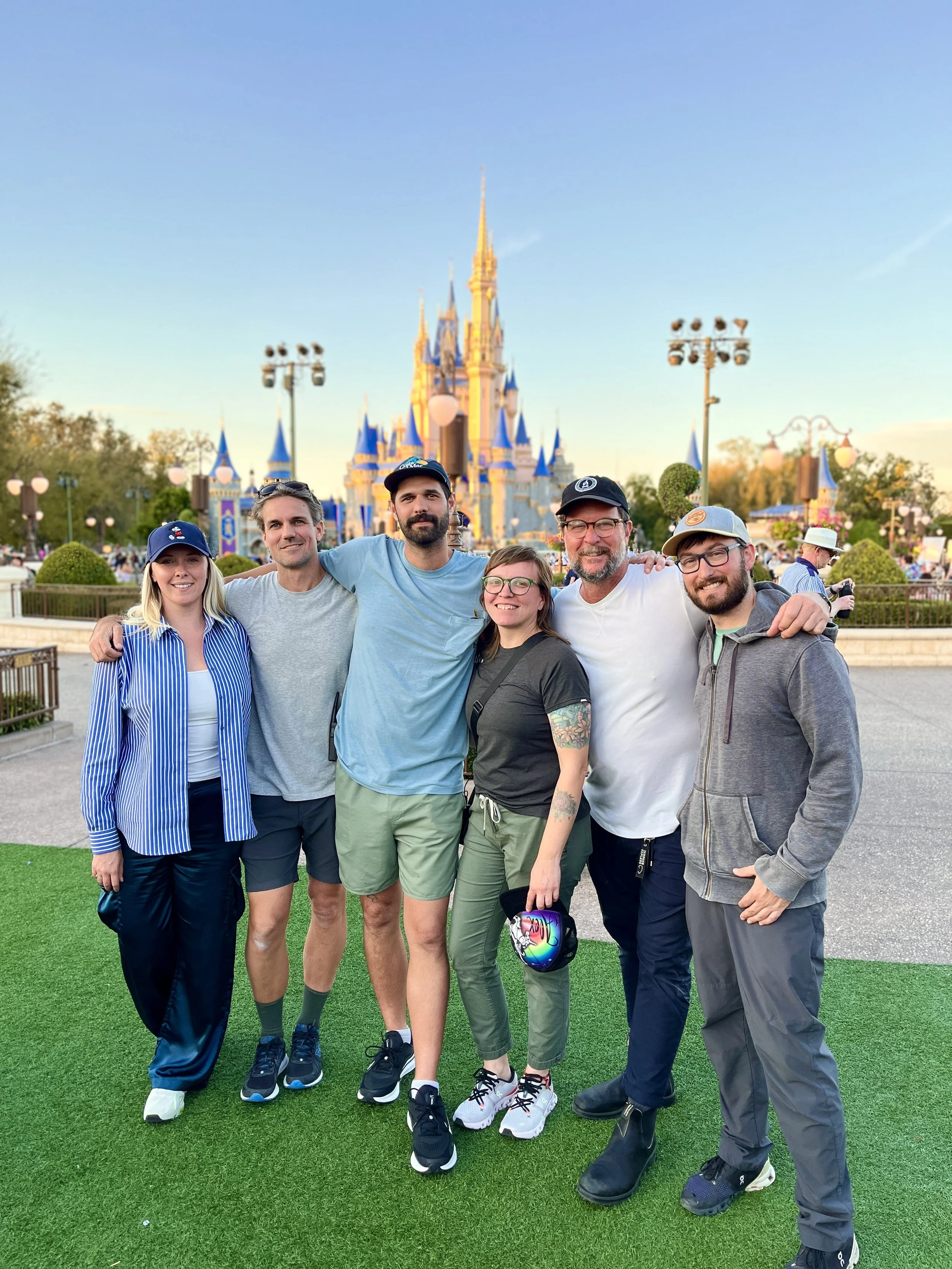 Group of six friends standing together at Disneyland, smiling with Cinderella Castle in the background during daytime on a photoshoot.