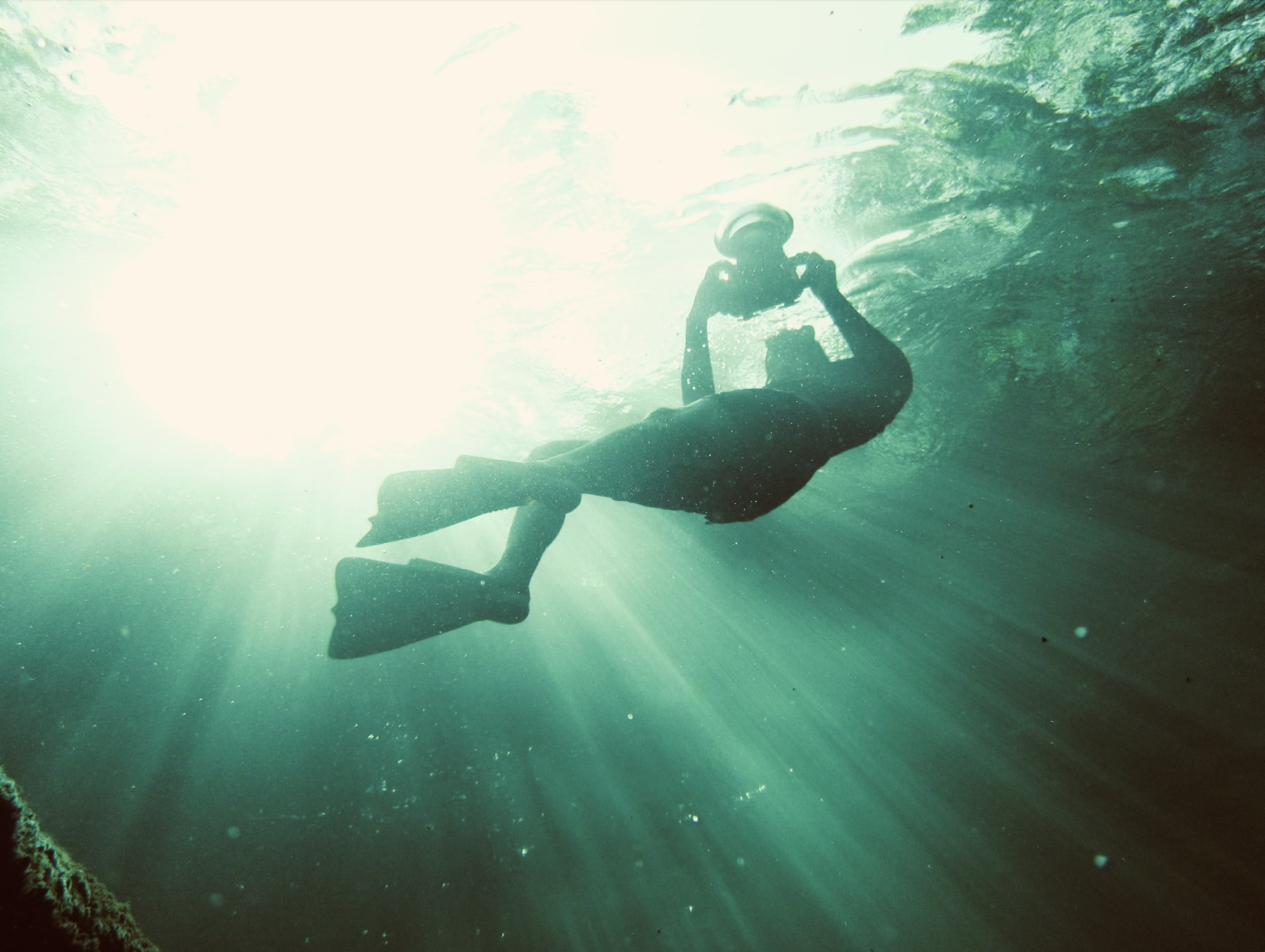 Lloyd Wilkinson, editorial & underwater photographer, swimming underwater with fins and a mask, sunlight rays streaming through the water.