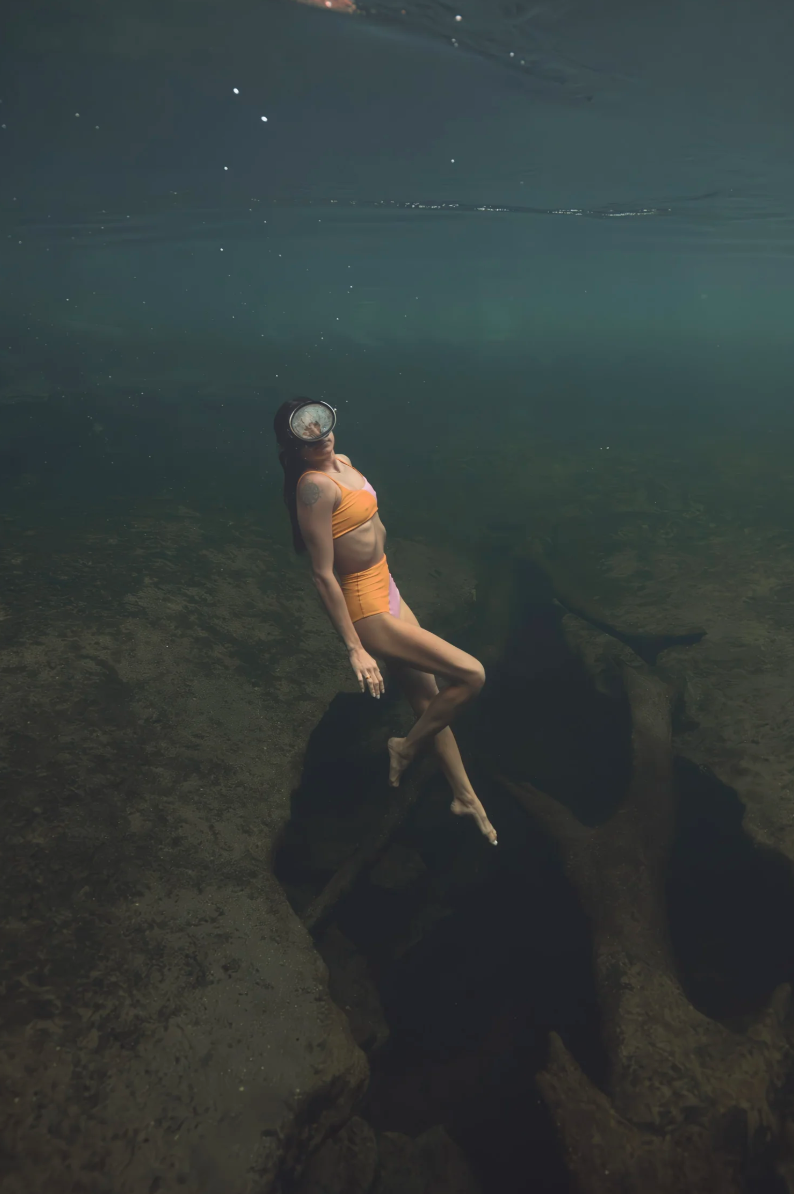 Editorial photo series of a woman in an orange bikini freediving above the rocks in a Florida spring.