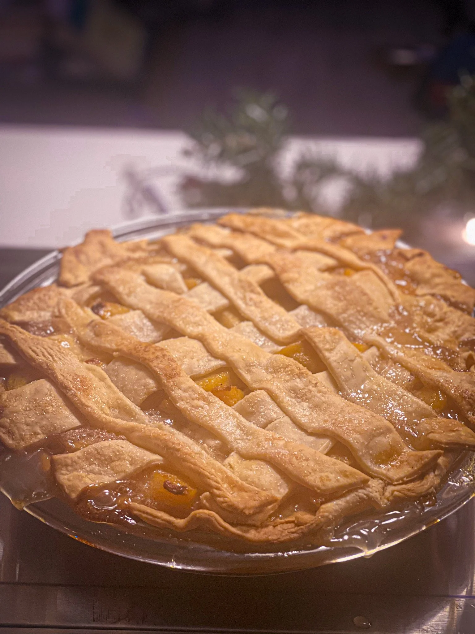 A freshly baked peach pie with a lattice crust on a glass pie dish, sitting on a stovetop or counter.