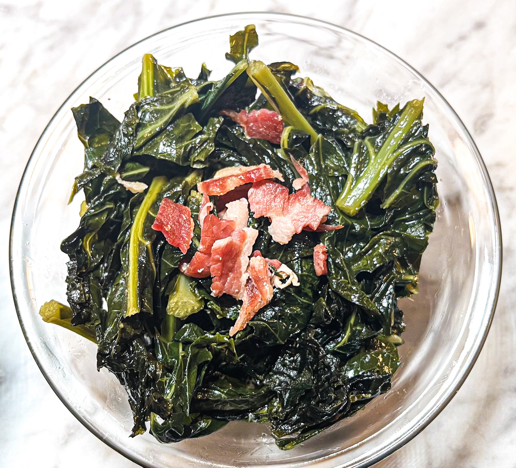 Cooked kale topped with chopped bacon in a glass bowl.