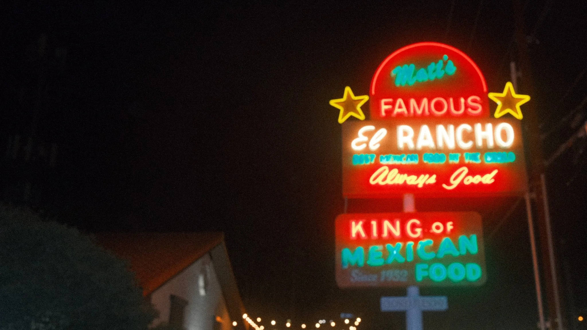 Colorful neon sign advertising a Mexican restaurant called 'El Rancho,' stating it is the most Mexican food in the world and a king of Mexican food since 1952, with stars and text in red, green, and blue against a dark night sky.