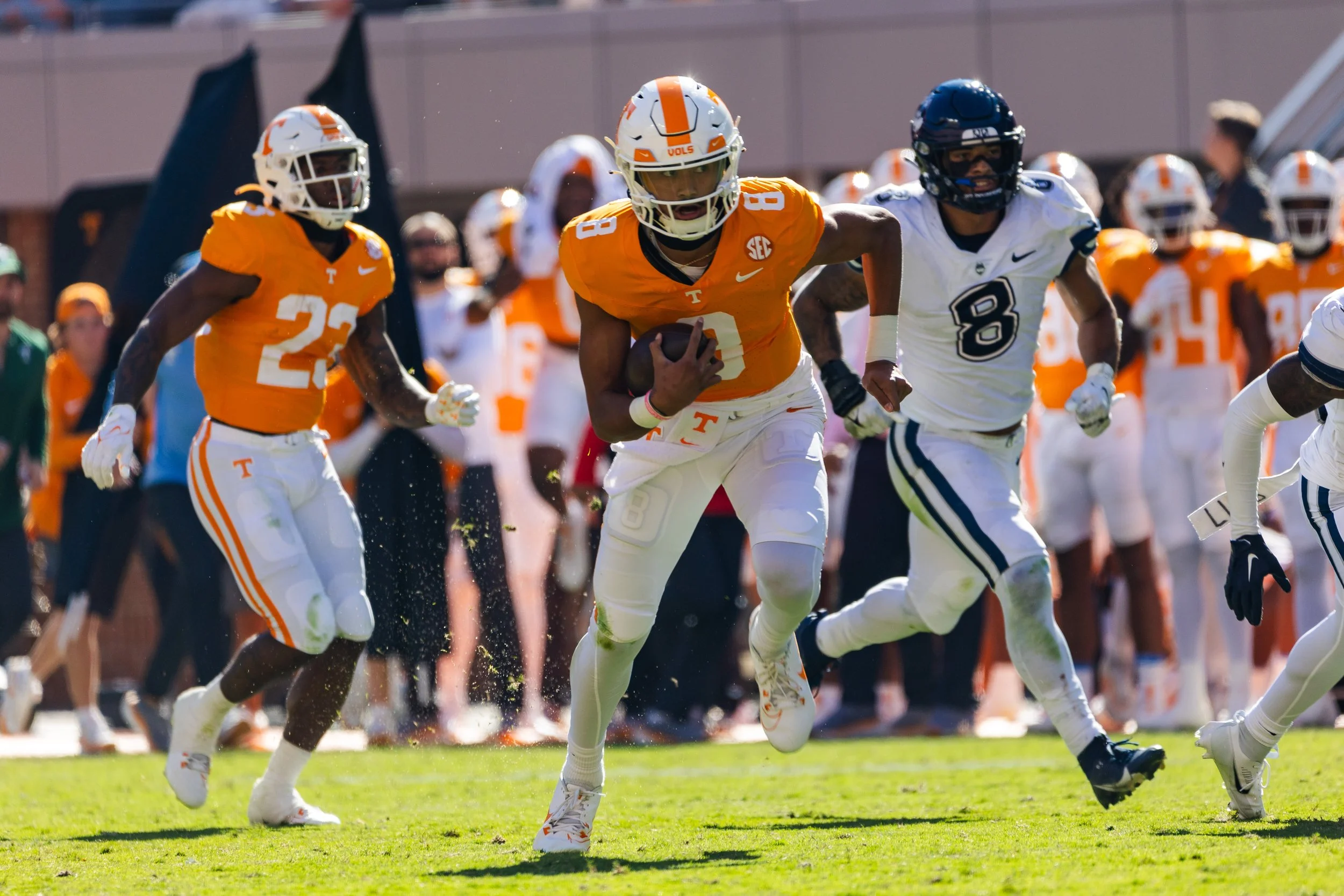 Football game with players in orange and white uniforms, with one player holding the football and running.