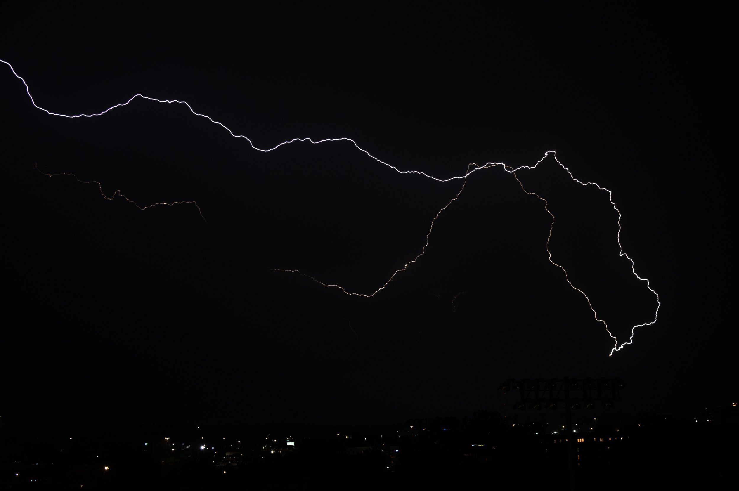 Lightning bolts streak through a dark night sky over a cityscape.