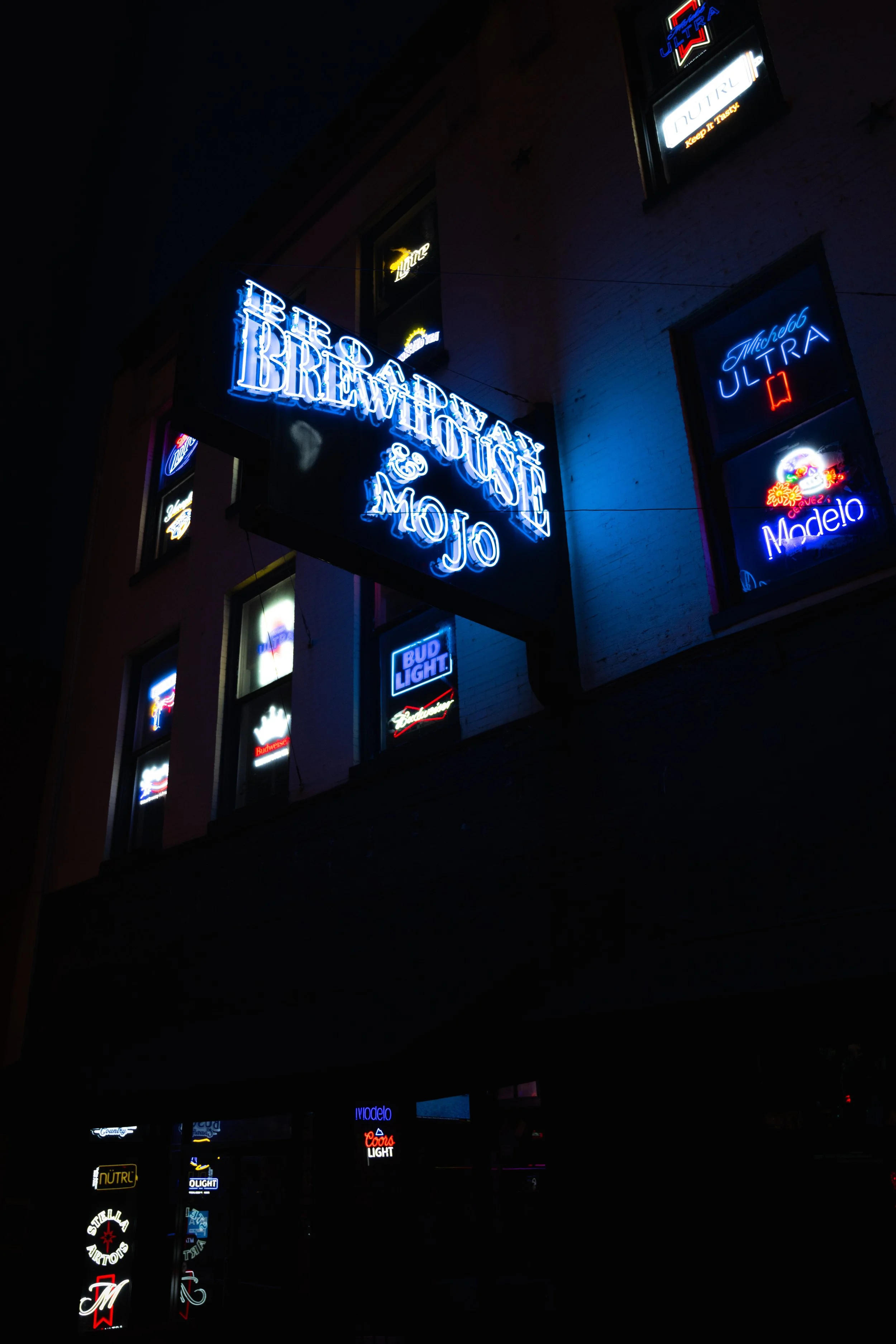 Nighttime view of a building with multiple neon signs, including a prominent sign that reads 'The Breakfast & Mojo'