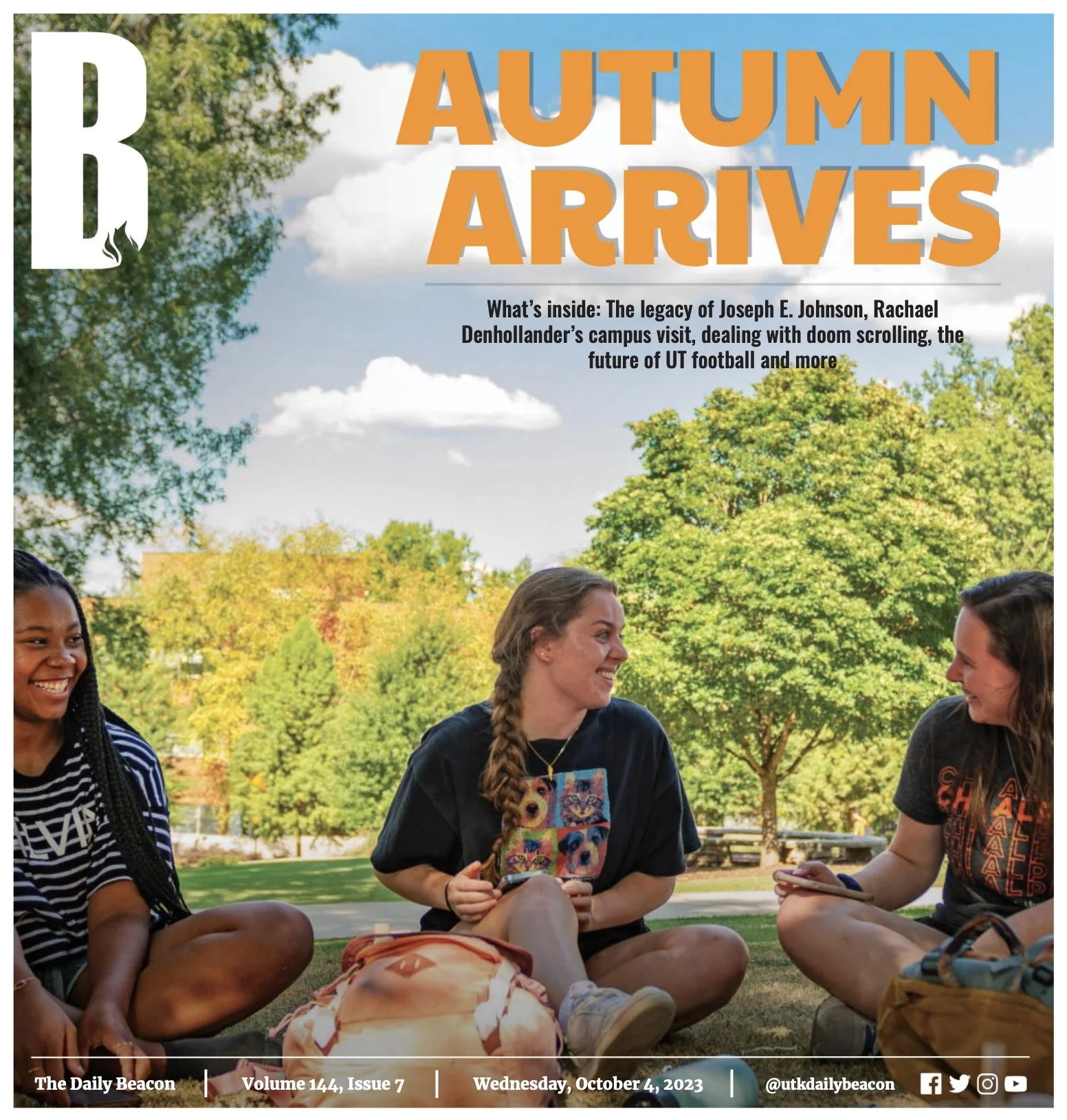 Three young women sitting on grass outside, smiling and talking in fall weather with trees and a bright sky in the background.